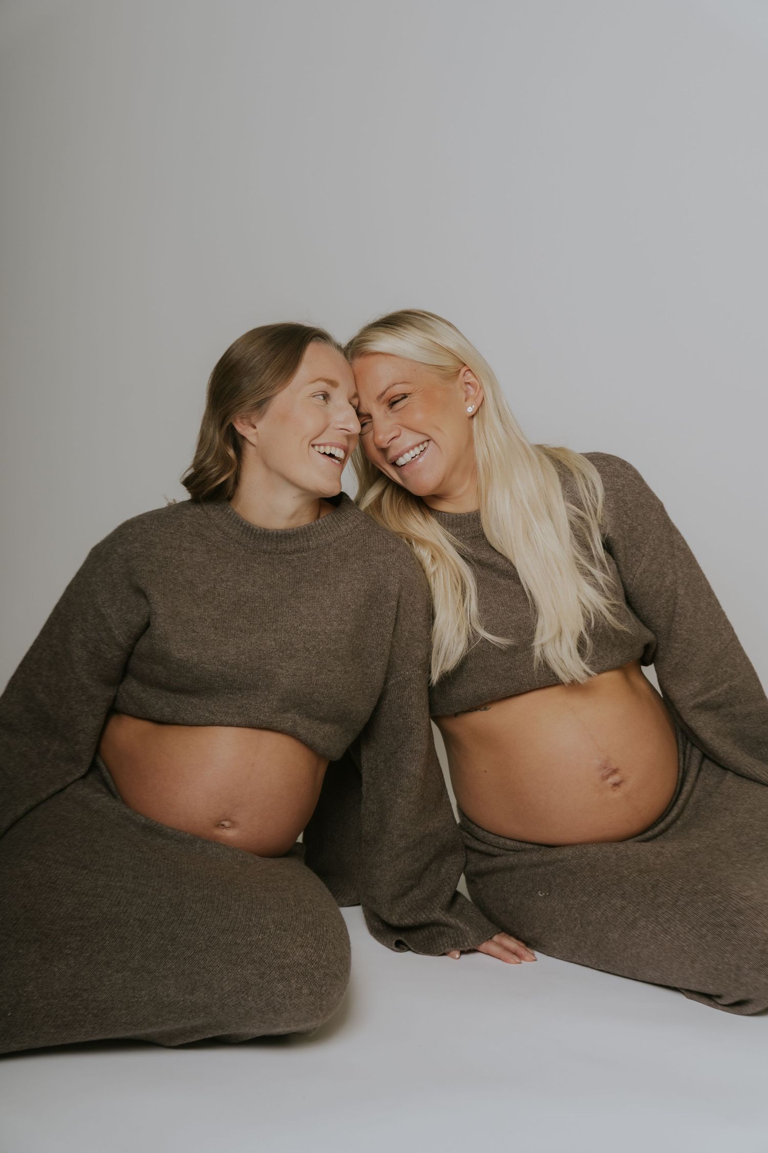 Two people in matching brown sweaters share a candid moment during a minimalist studio photoshoot.