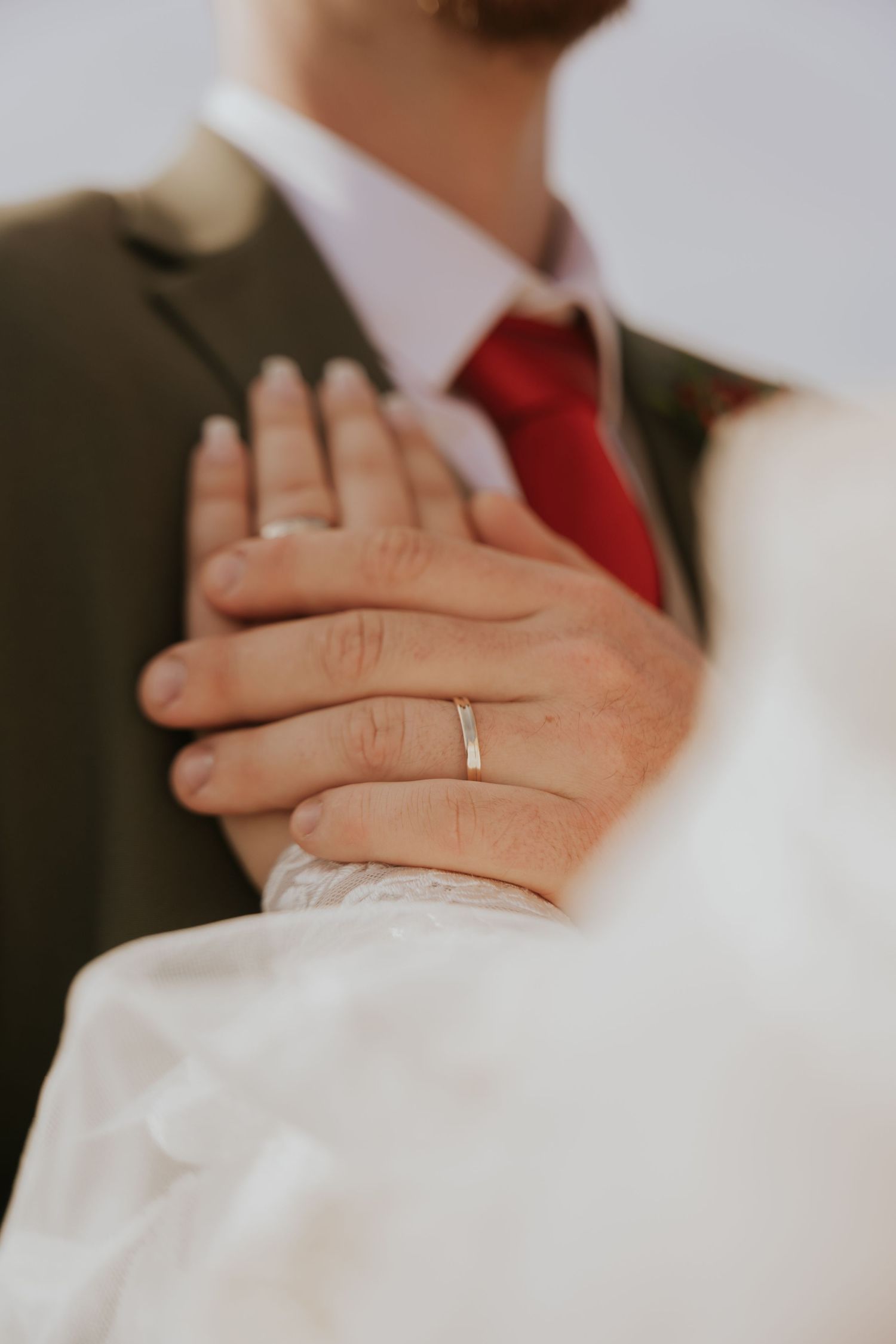 Close-up detail of newlyweds' hands clasped together showing wedding rings.