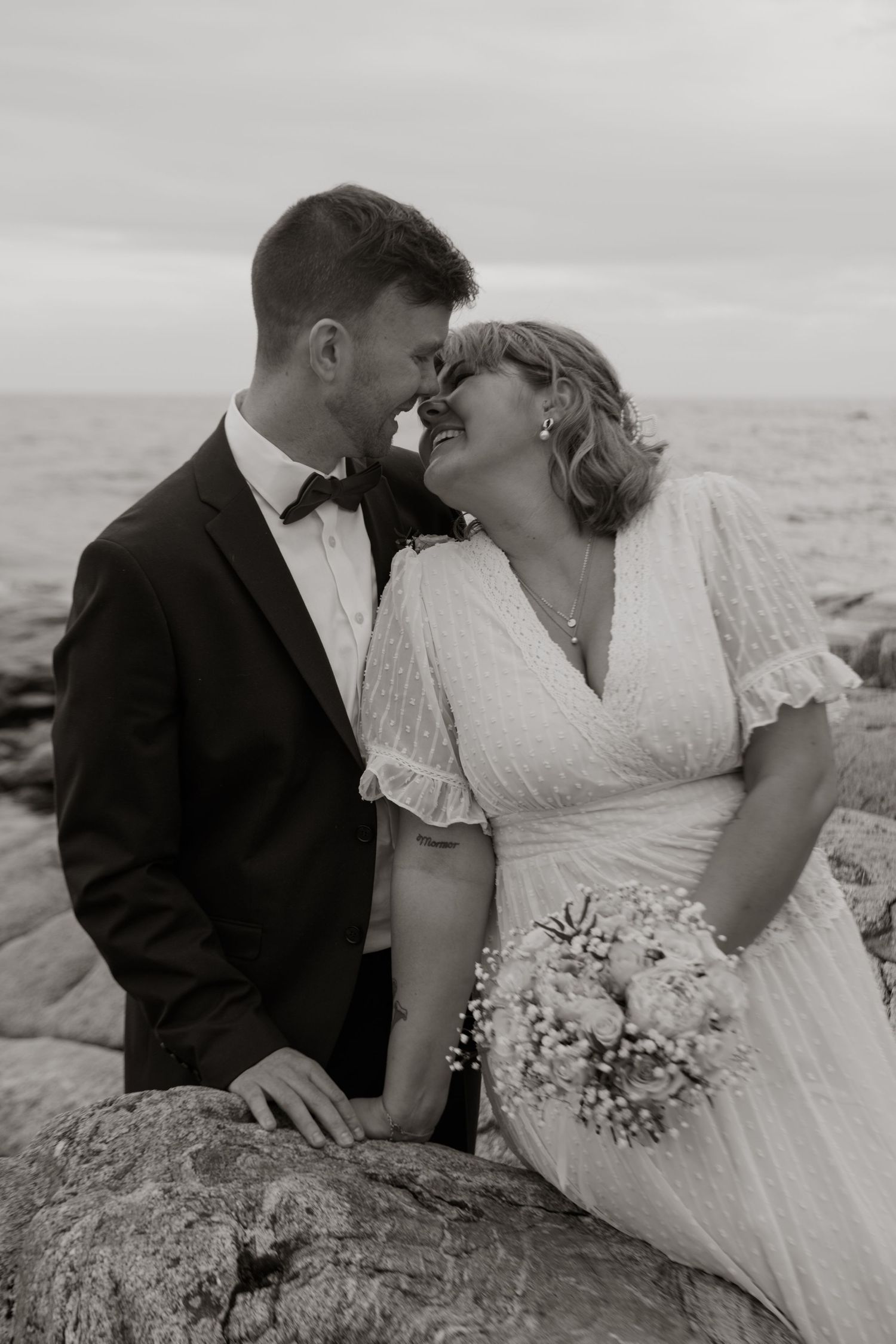 Black and white wedding portrait of couple embracing on seaside rocks.