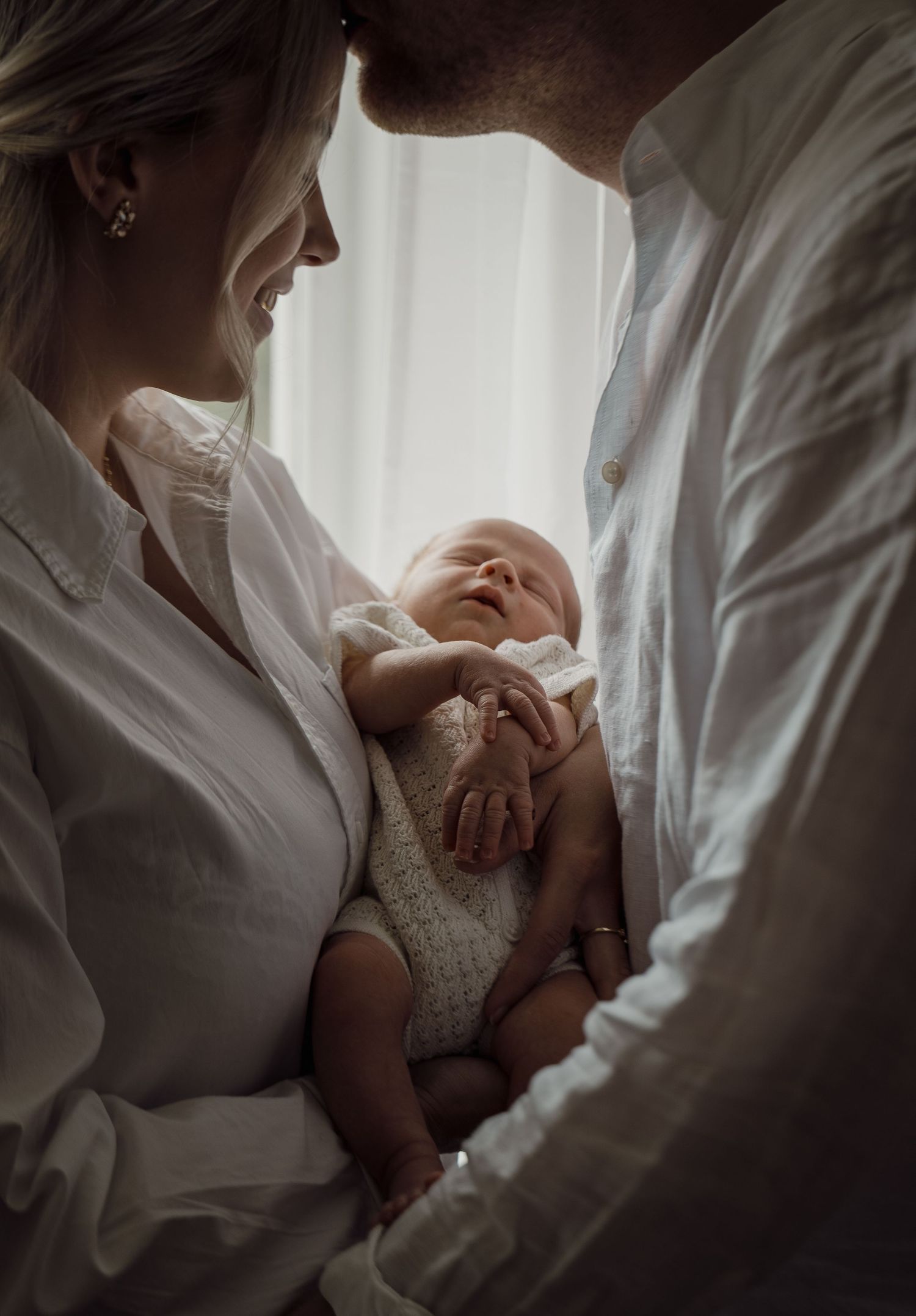 A tender moment between parents and their newborn baby captured in gentle window light.