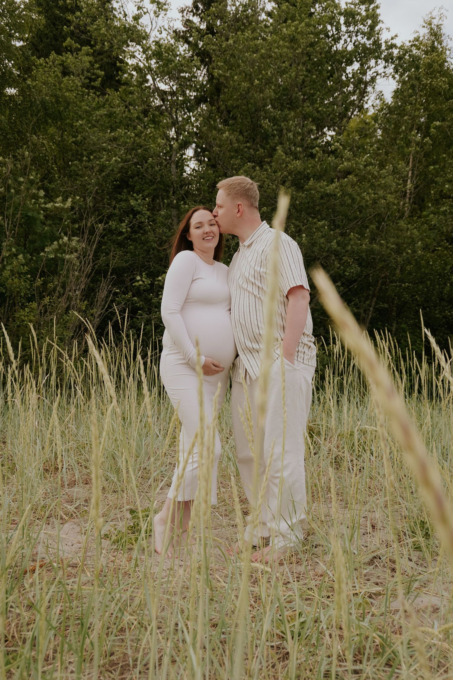 Couple in white outfits sharing intimate moment in tall grass field.