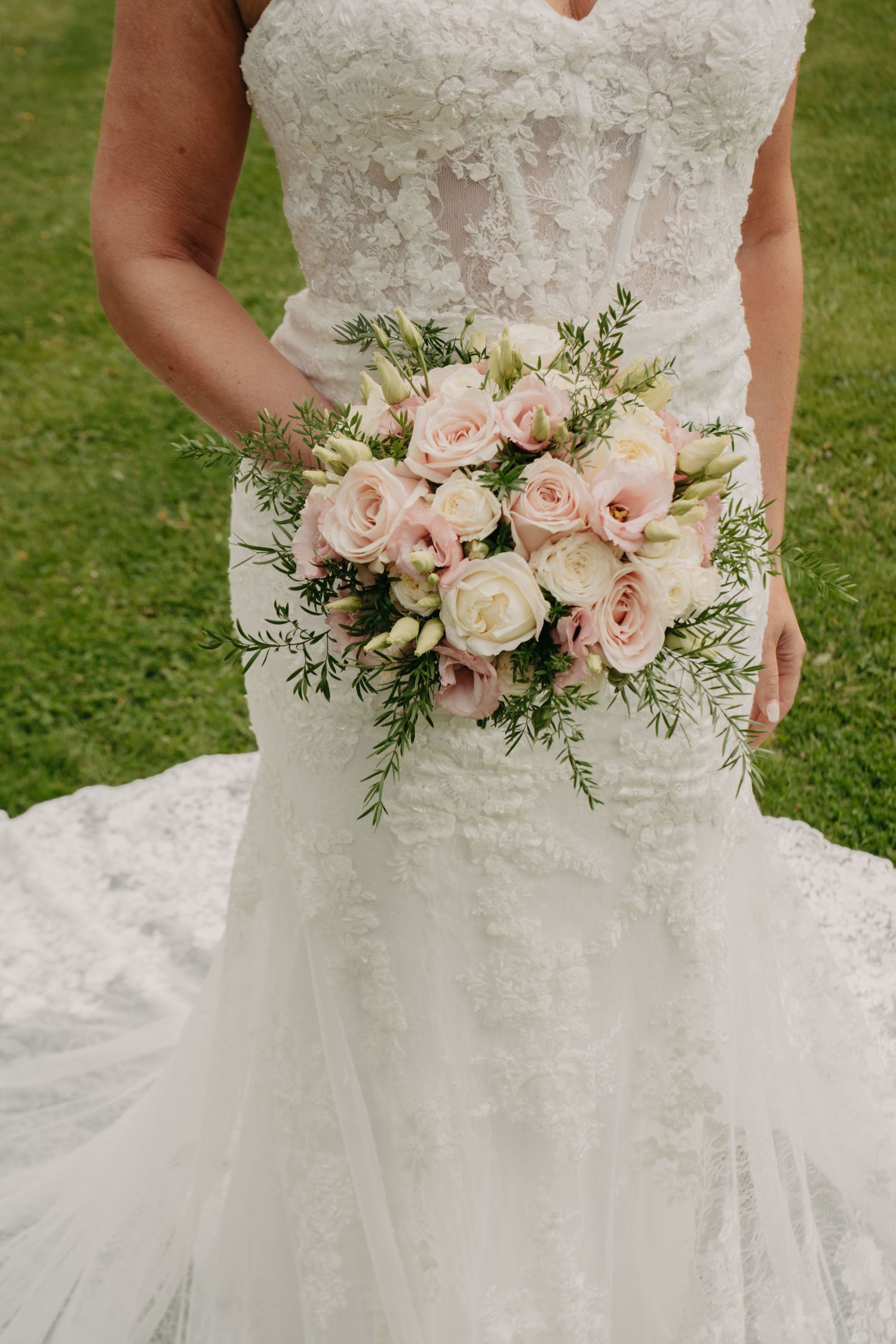 Elegant bridal bouquet of blush pink and white roses against a lace wedding dress.