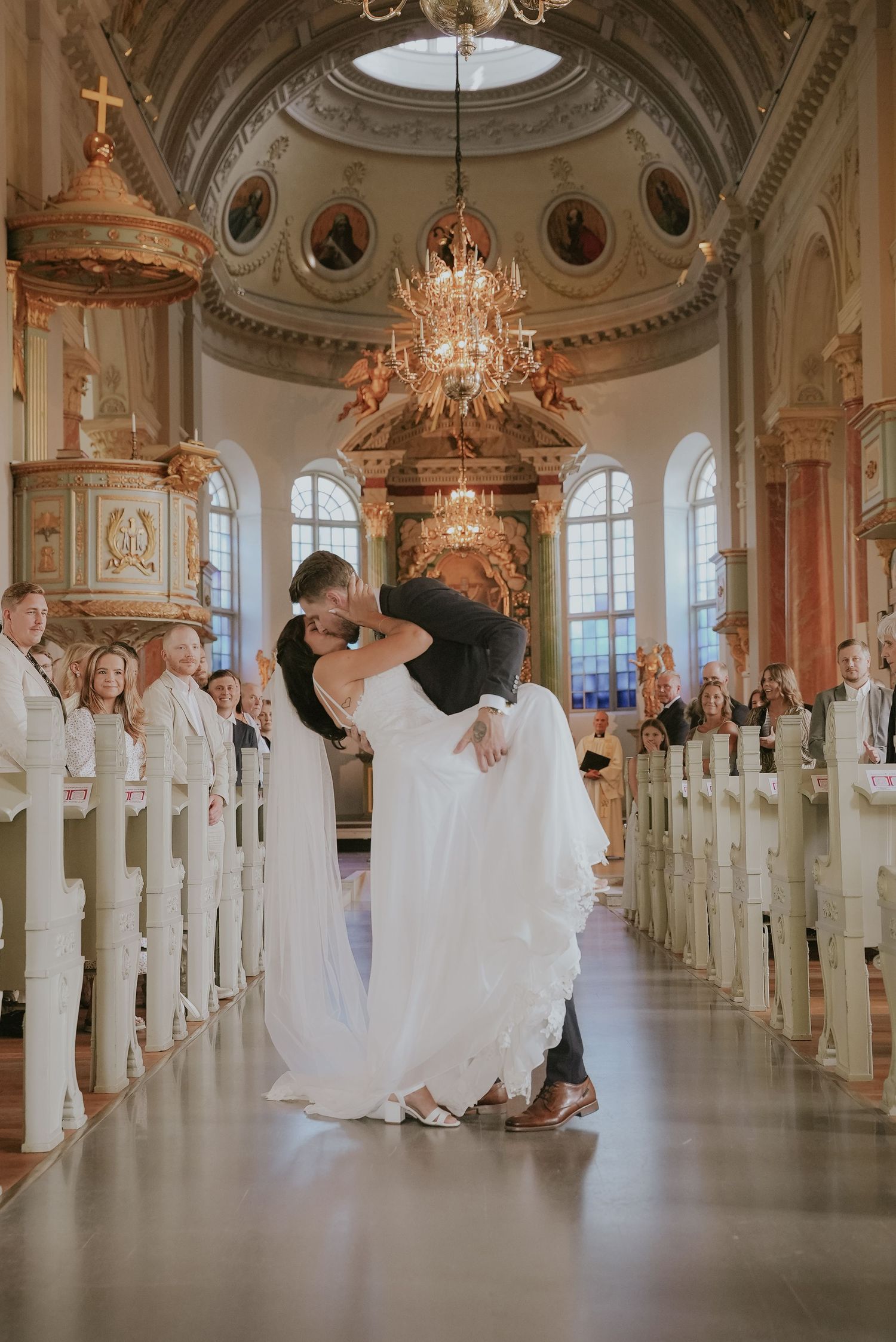 Elegant wedding ceremony venue with ornate chandeliers and white-draped chairs in a grand ballroom with classical architecture.
