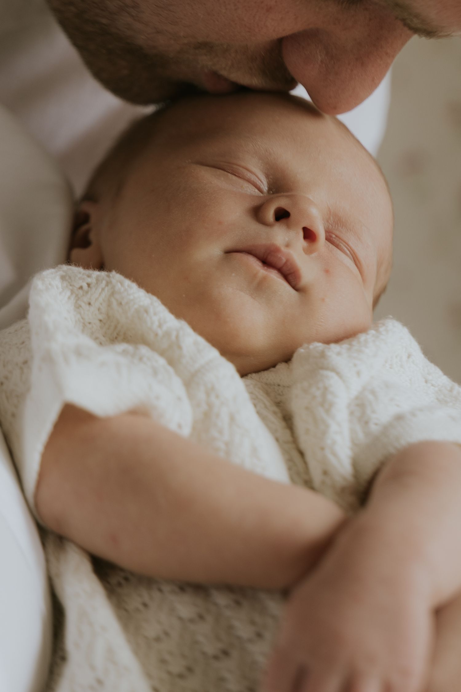 A sleeping baby wearing white lace clothing lies peacefully against a light background.