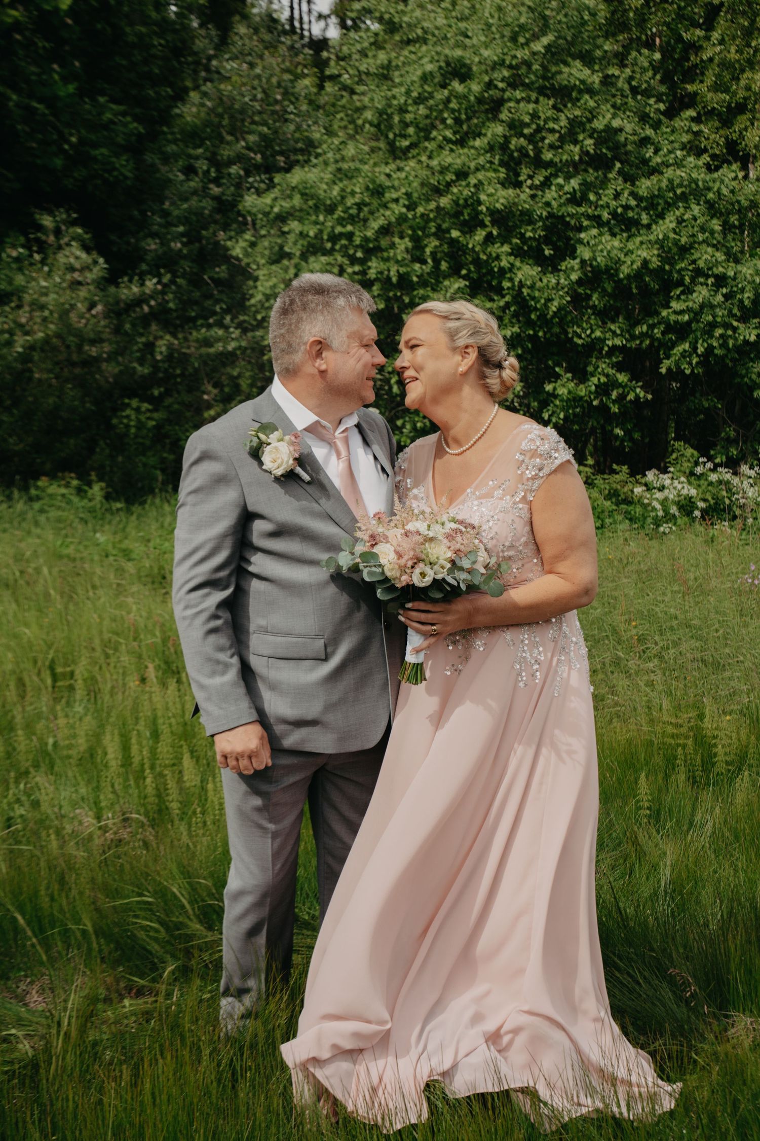 Wedding couple shares intimate moment in lush green meadow wearing blush and gray.