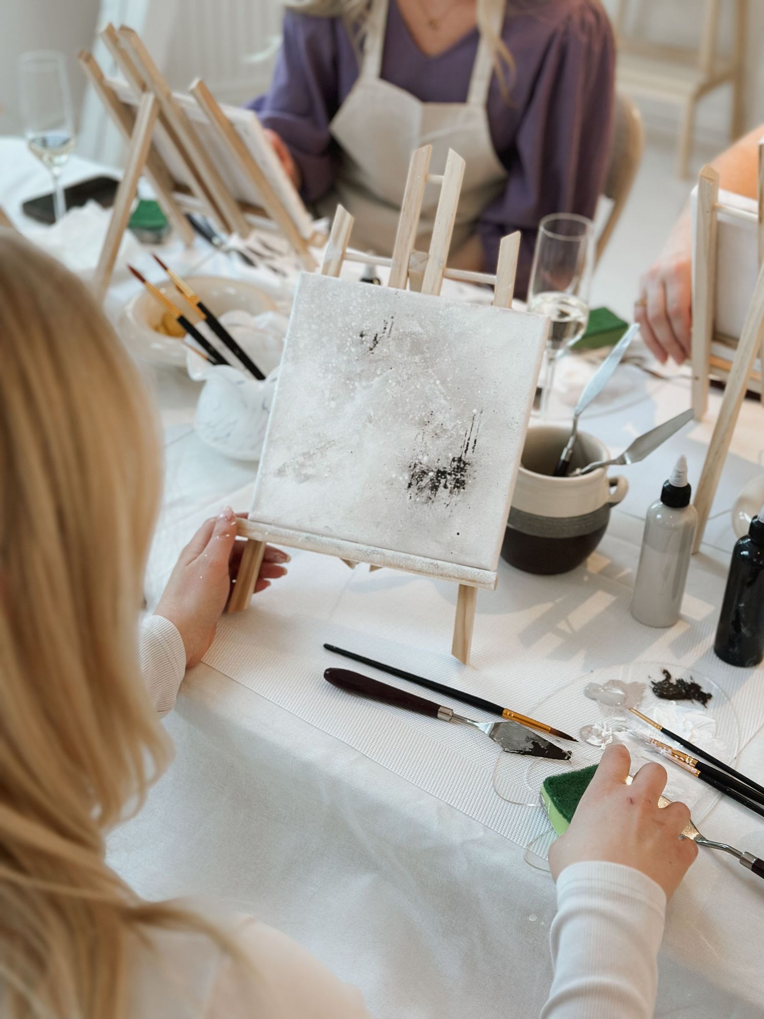 A person works on a detailed watercolor painting at a desk with art supplies and brushes spread out.