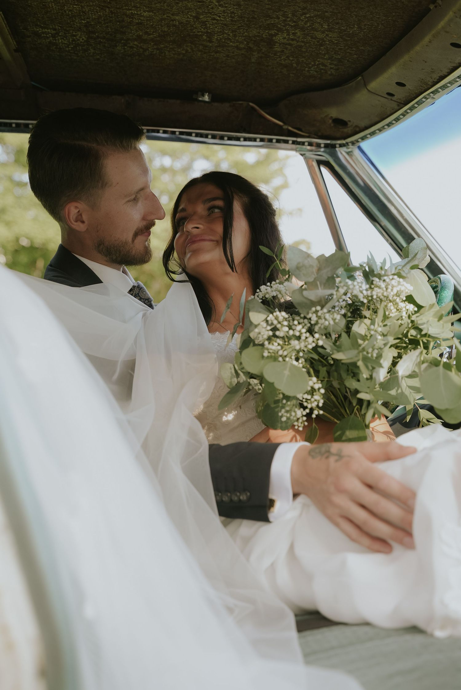 A tender moment between newlyweds in a car with white floral decorations and a flowing veil.