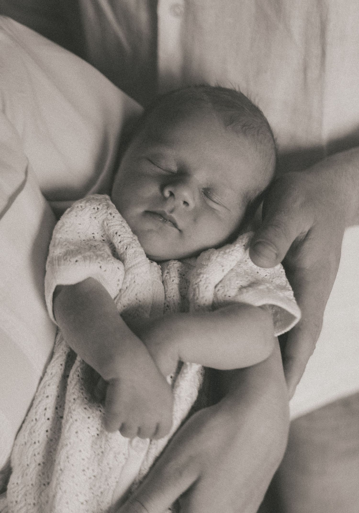 A series of black and white photographs showing a sleeping newborn baby in different peaceful poses on white bedding.