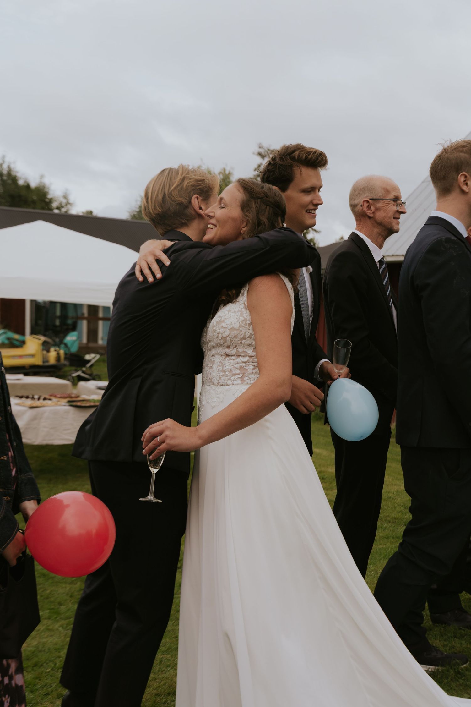 Wedding party celebrating outdoors with balloons and champagne on a cloudy day.