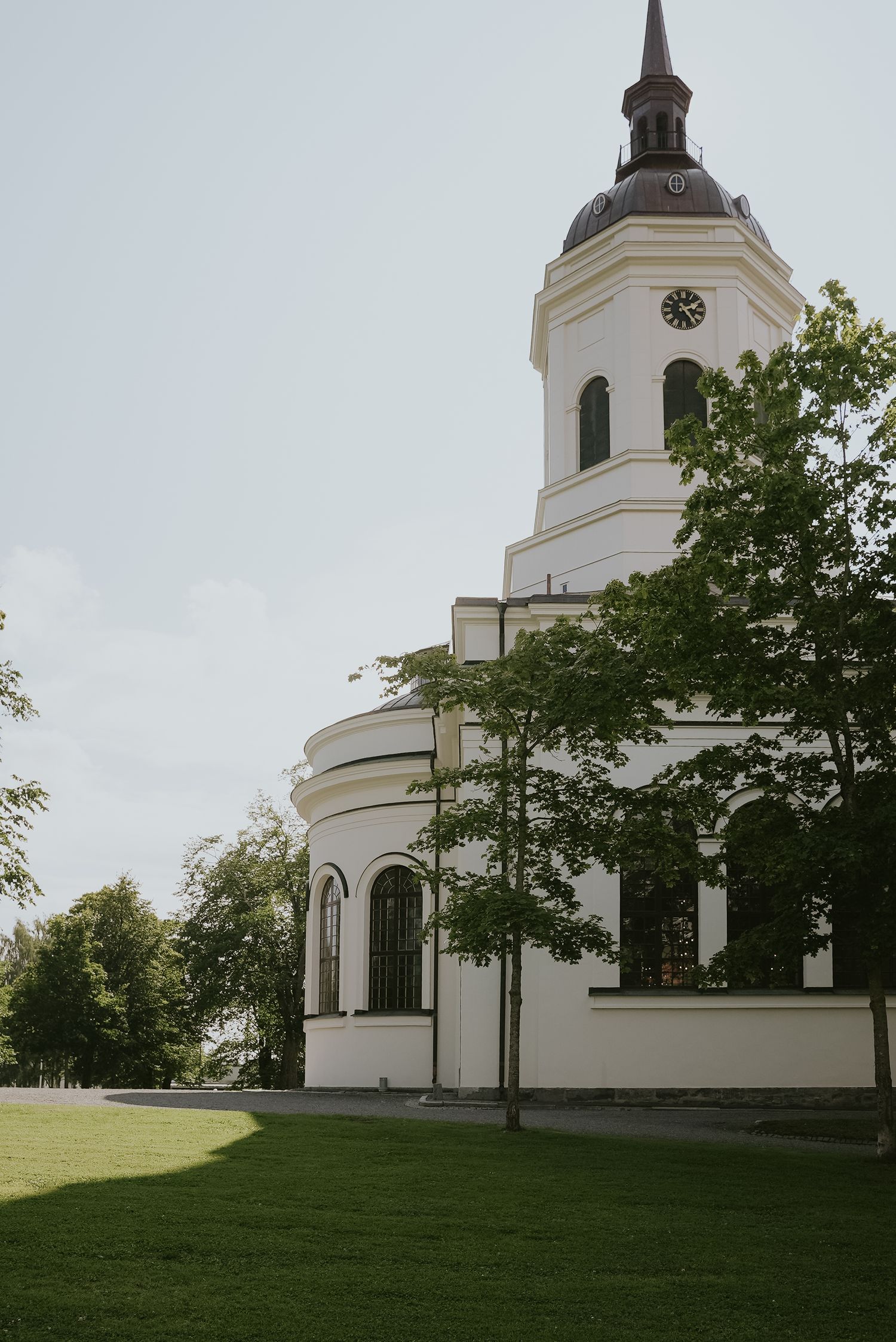 White church with bell tower and dome sits on manicured lawn surrounded by trees on an overcast day.