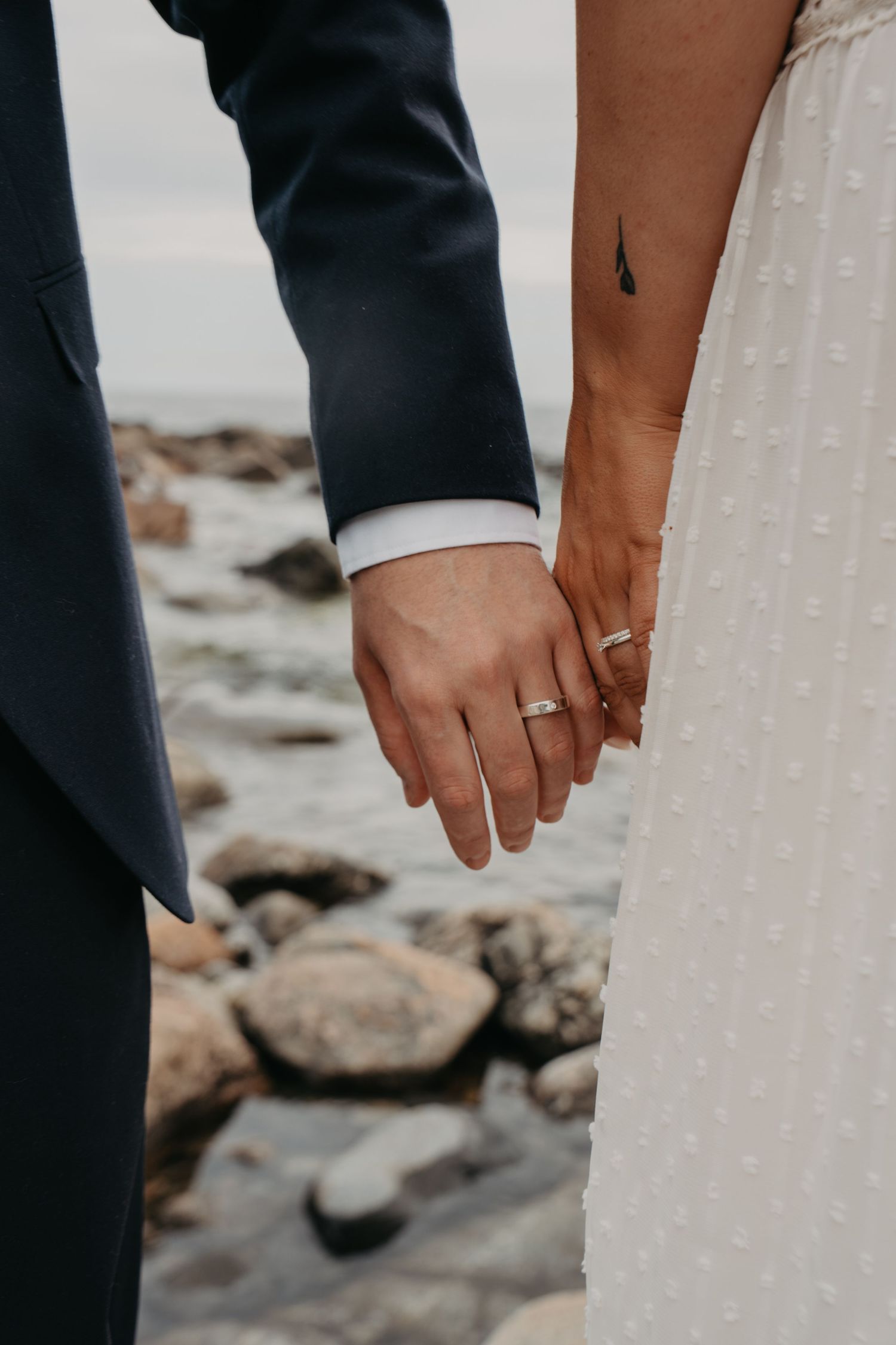 Detail shot of newlyweds' hands with wedding rings against white dress.