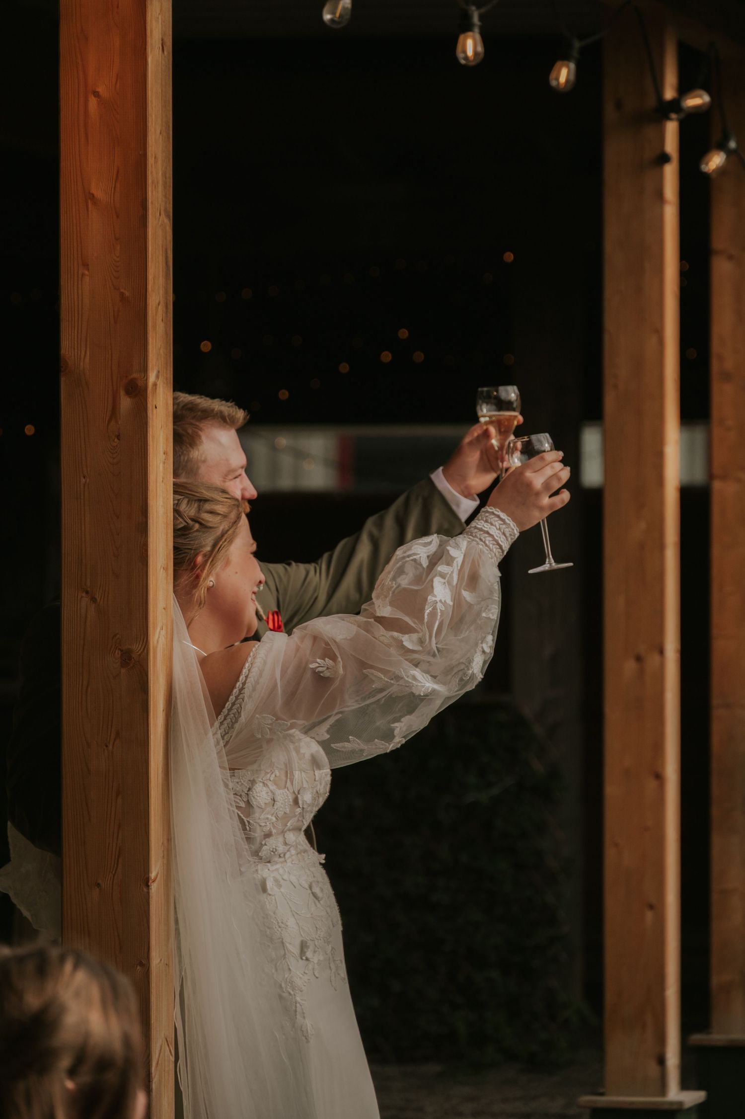 A couple shares a celebratory toast during their wedding reception in a rustic wooden venue.