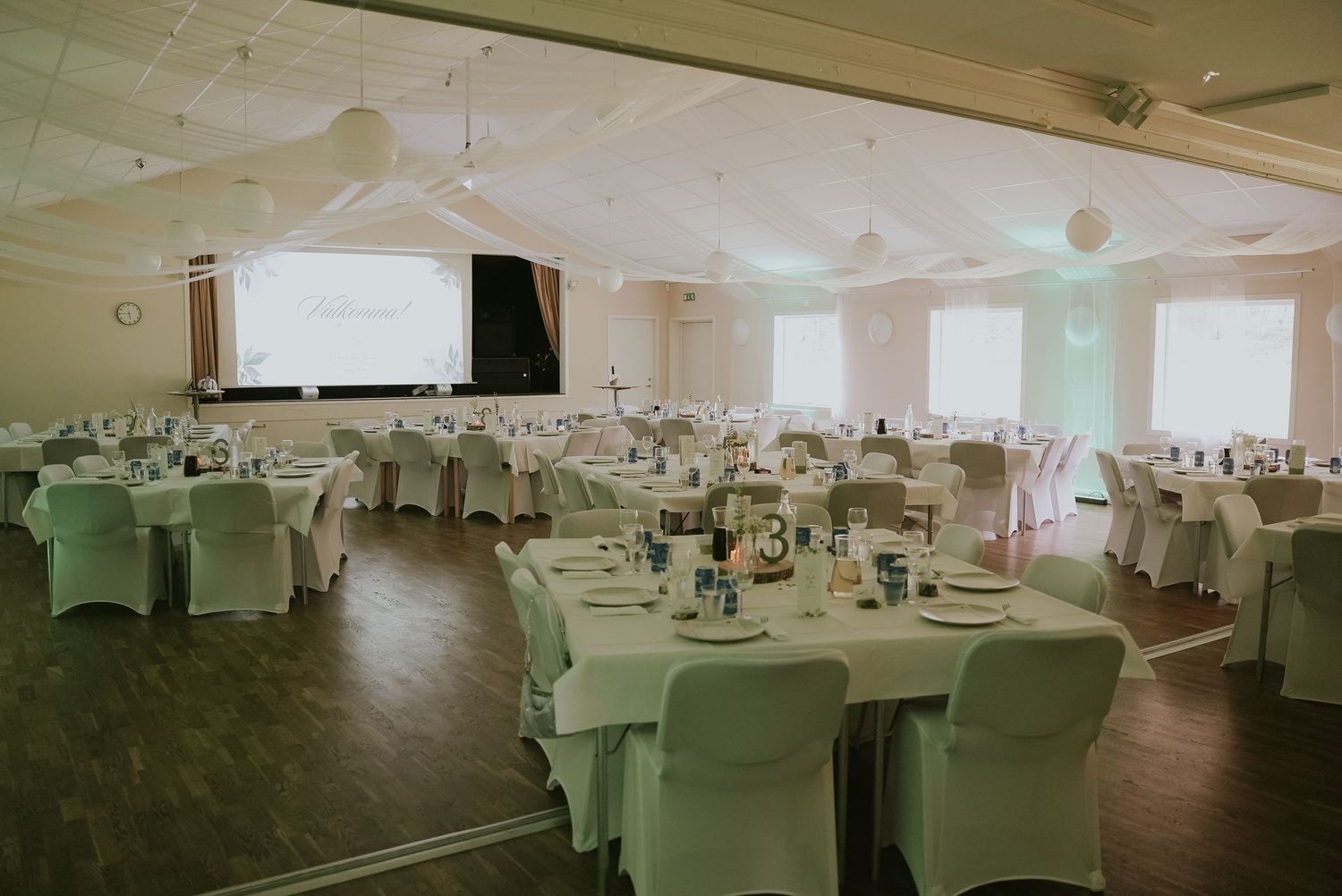 Large banquet hall with round tables covered in white linens and elegant place settings arranged for a formal event.
