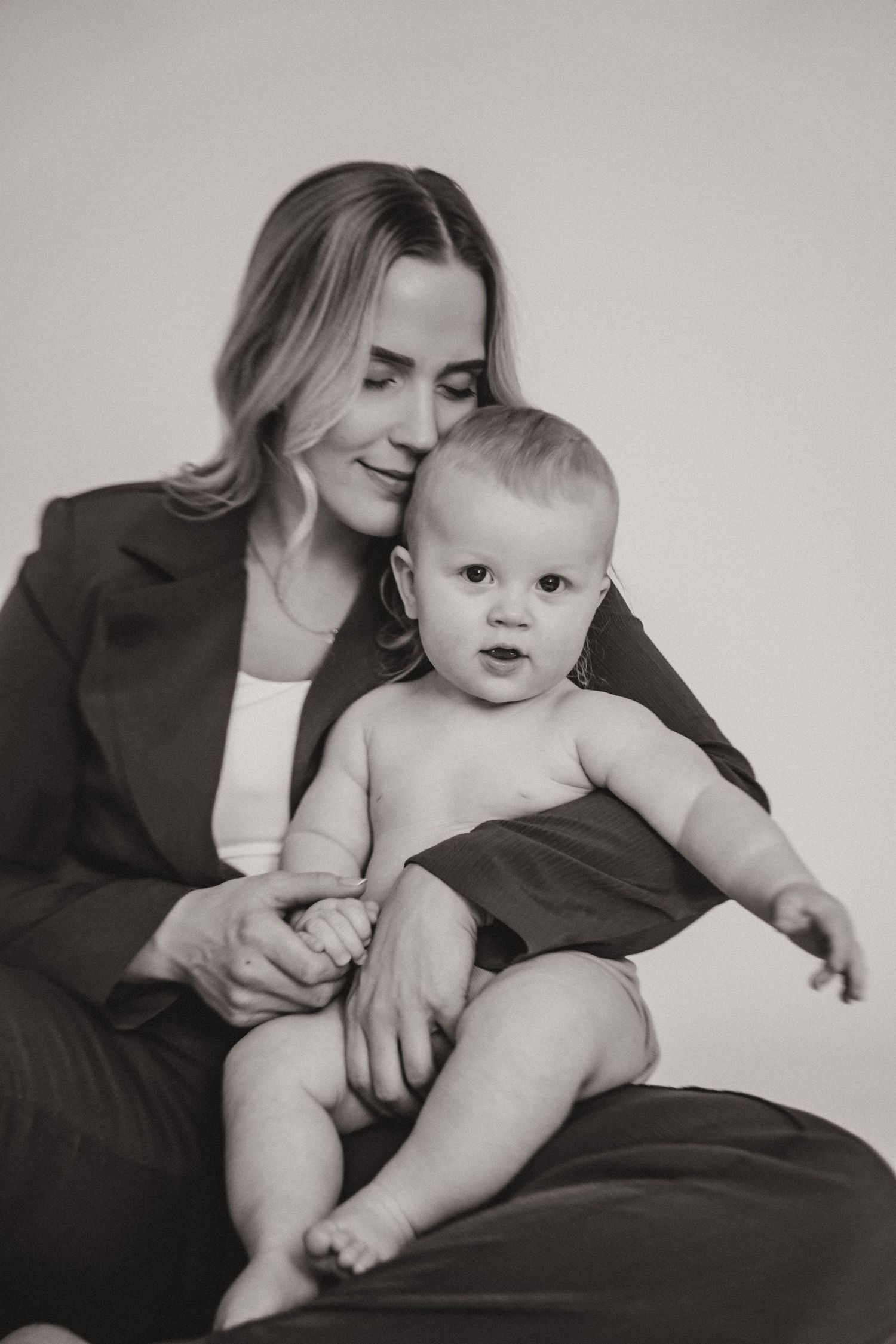 Black and white studio portraits showing tender moments between parent and baby on a couch.