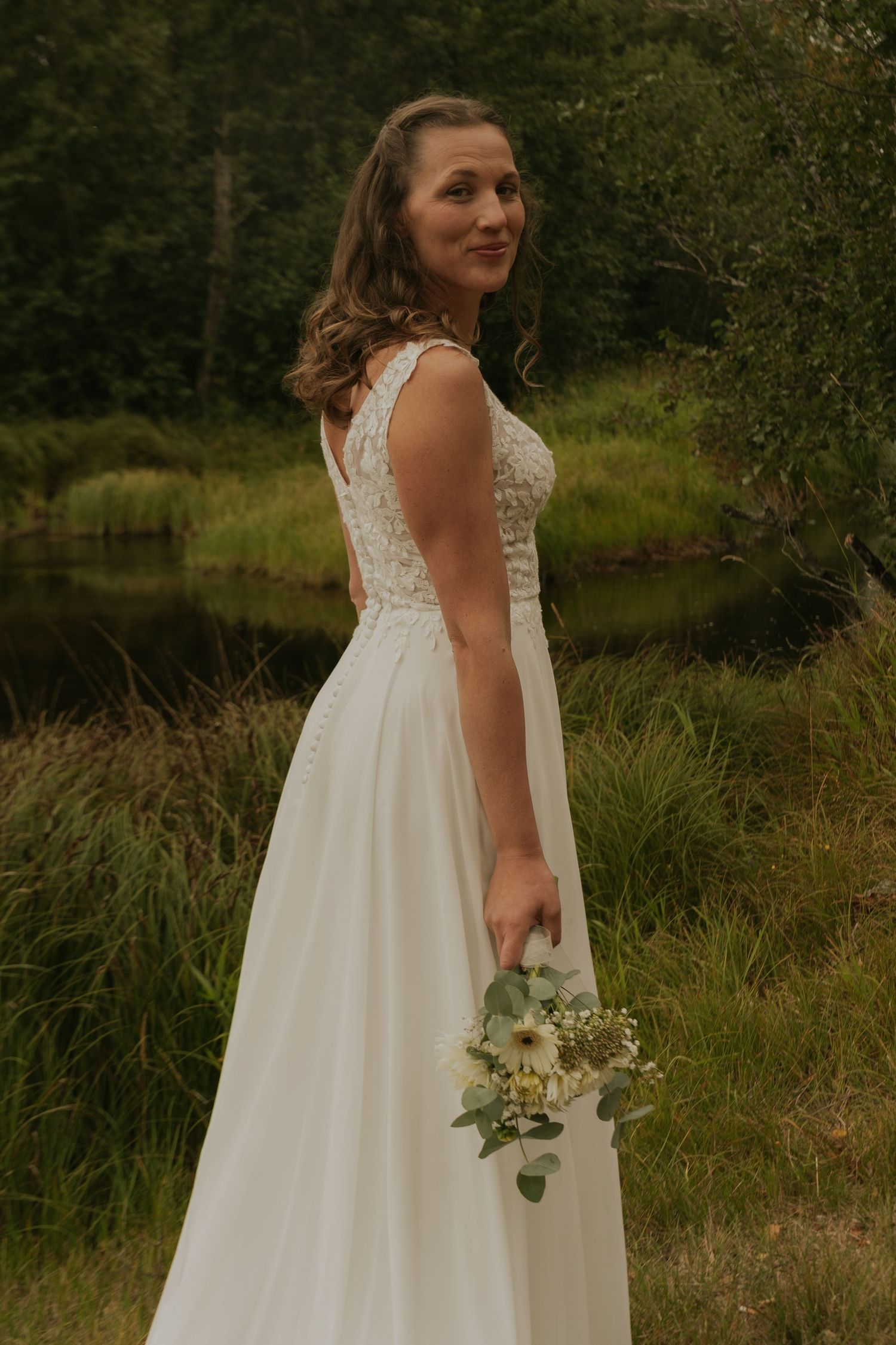 Bride in a flowing white dress holds a bouquet while posing in a rustic outdoor setting.