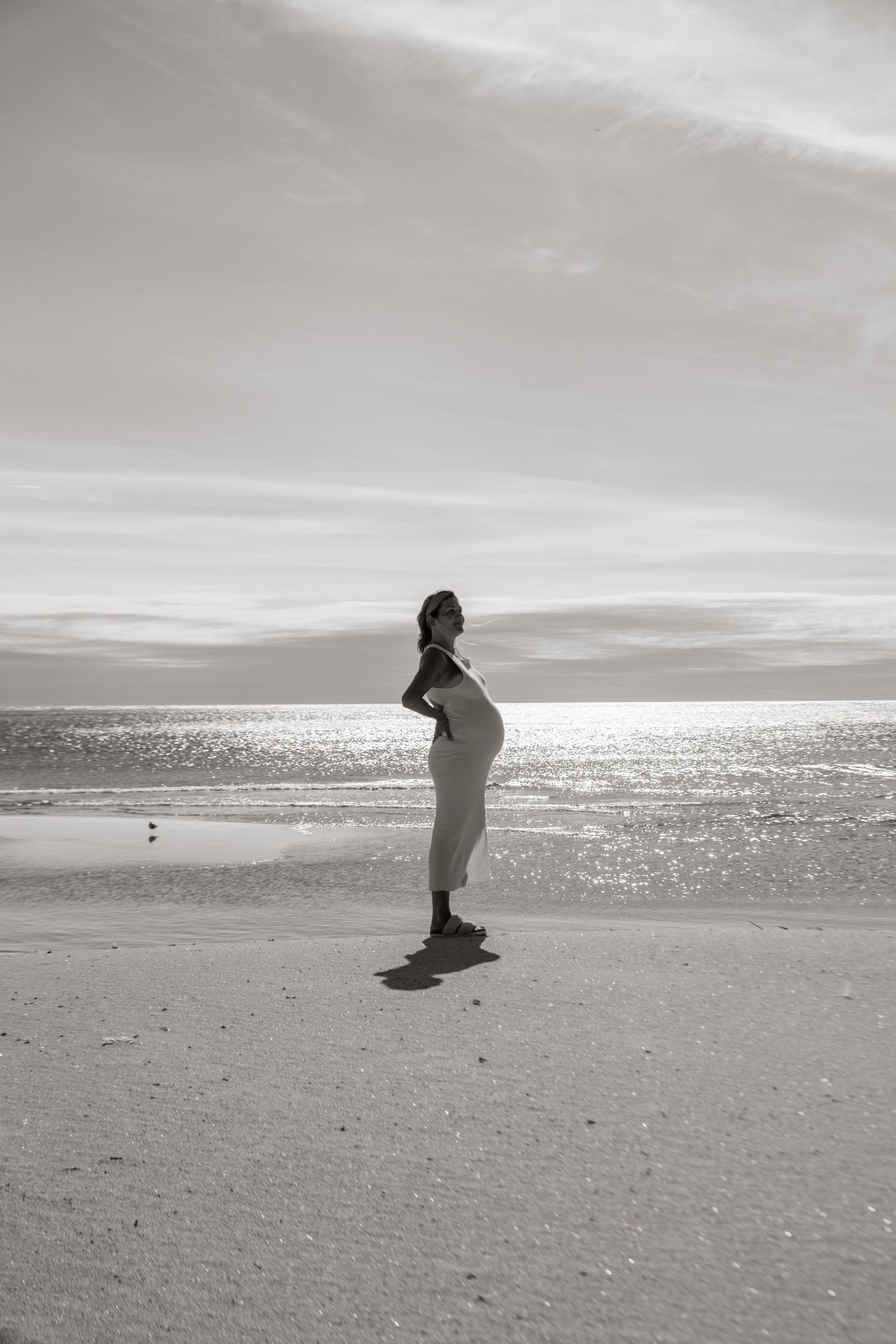 Black and white silhouette of person on empty beach at sunset.