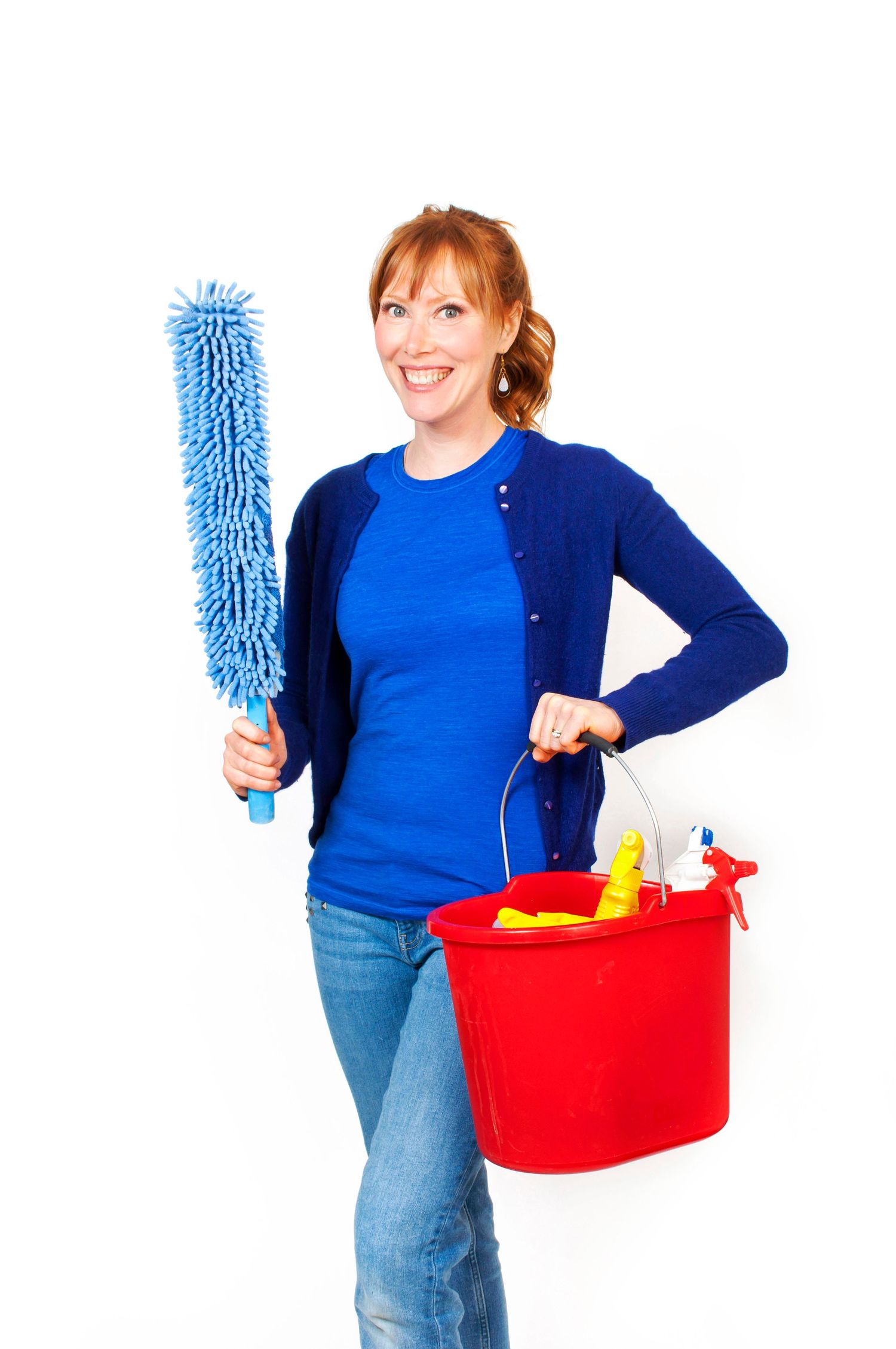Cheerful woman holding blue duster and red cleaning supply bucket on white background.