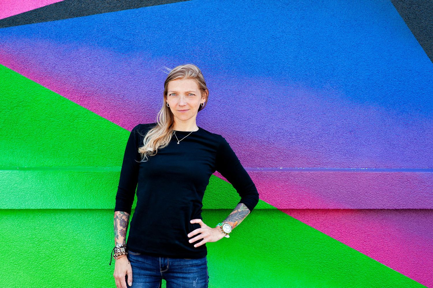 Woman in black long-sleeve top posing confidently before vibrant multicolored geometric wall.
