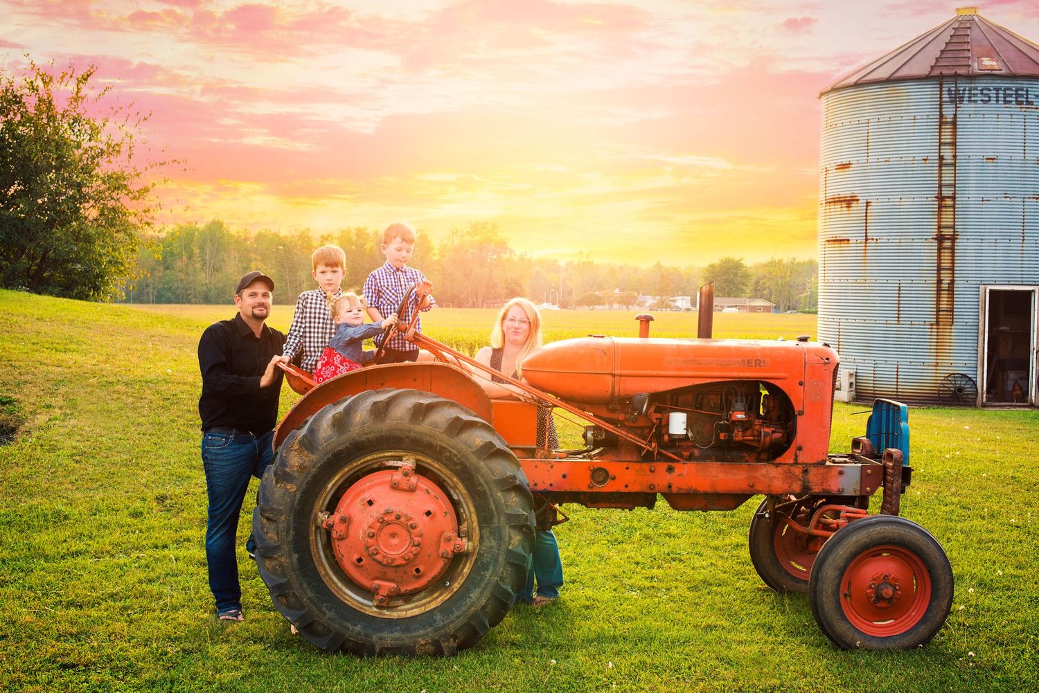 Family posing on a vintage orange tractor at sunset with a grain silo in the background.