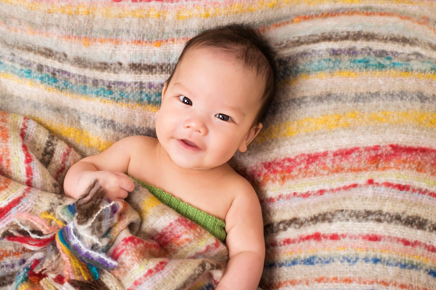 Smiling baby lying on a colorful striped blanket during a newborn photo session.