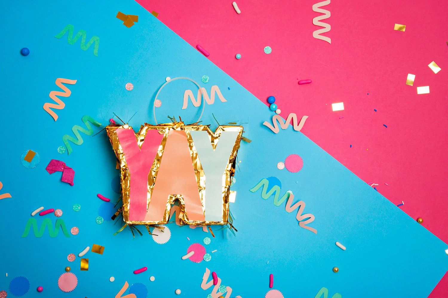 Pink letter YAY with gold glitter surrounded by colorful confetti on a blue and pink background.