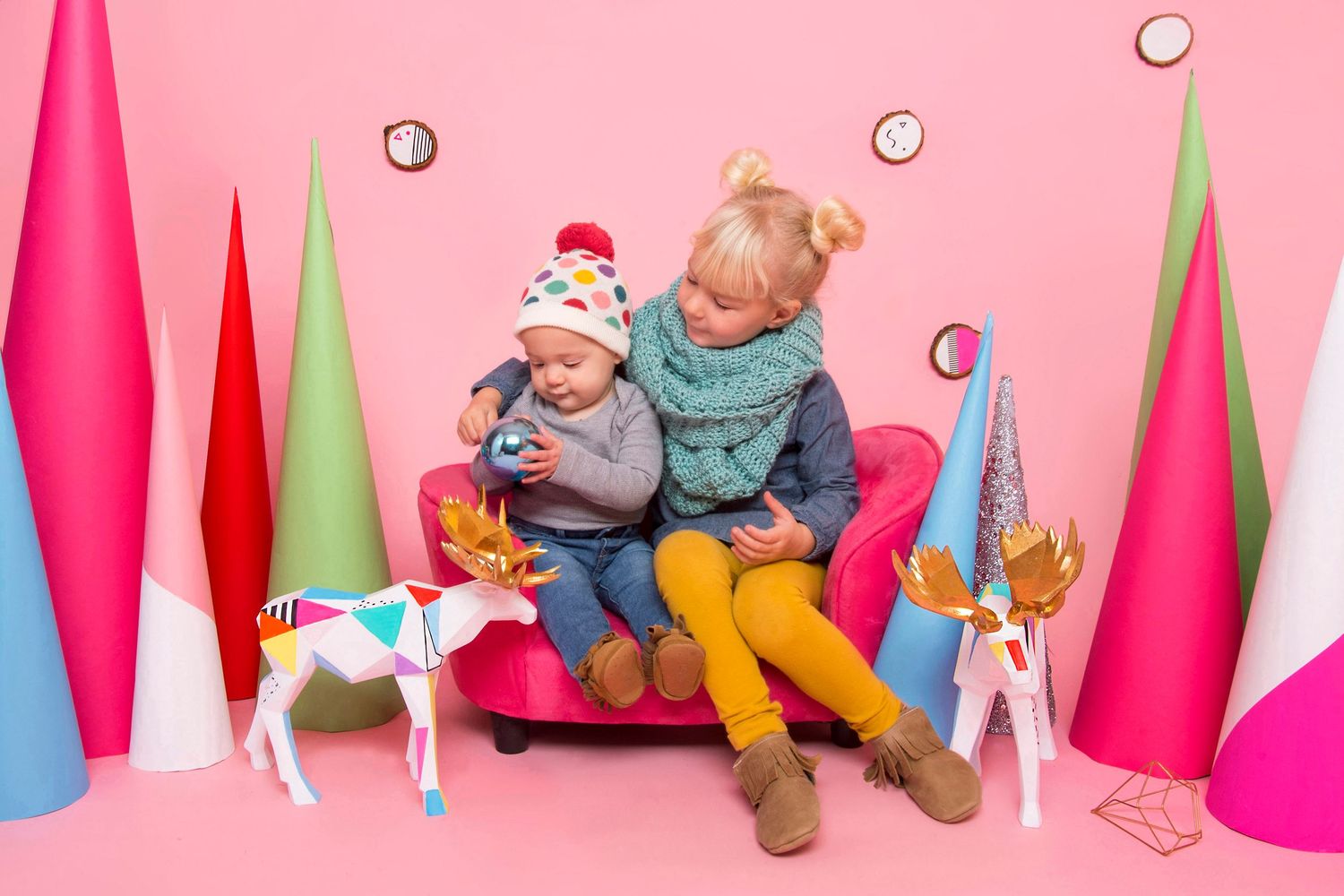 Sisters on pink sofa with baby surrounded by colorful paper Christmas trees.