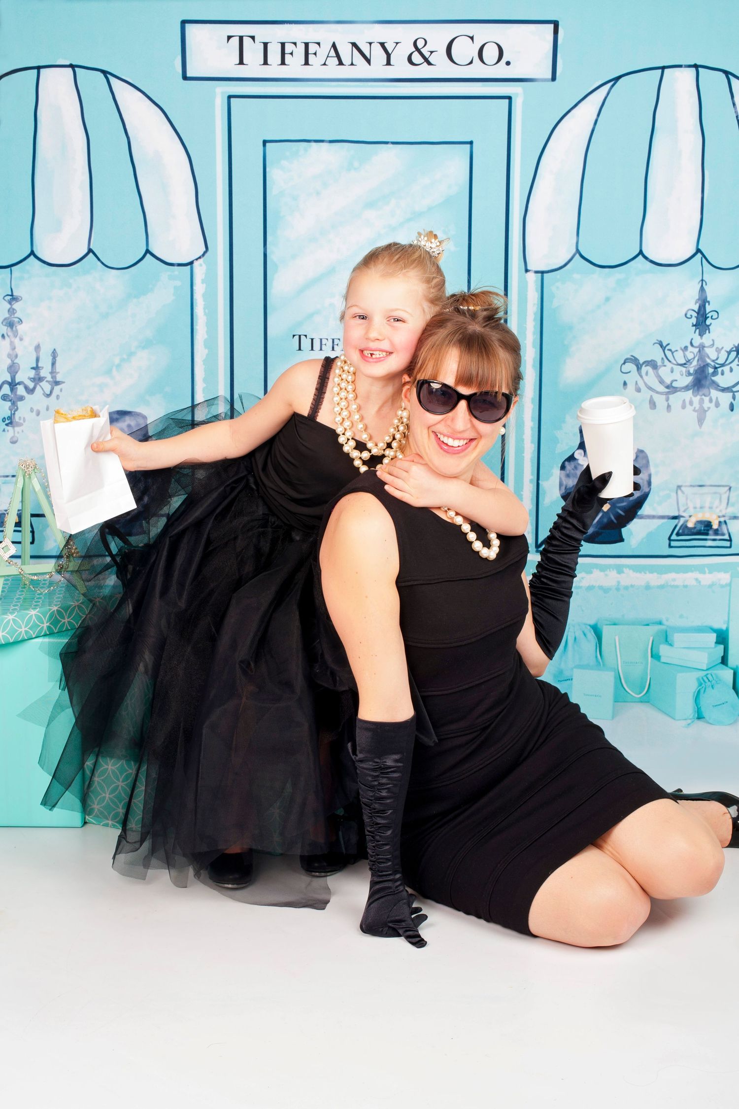 Mother and daughter in matching black dresses posing playfully in front of a Tiffany and Co backdrop.
