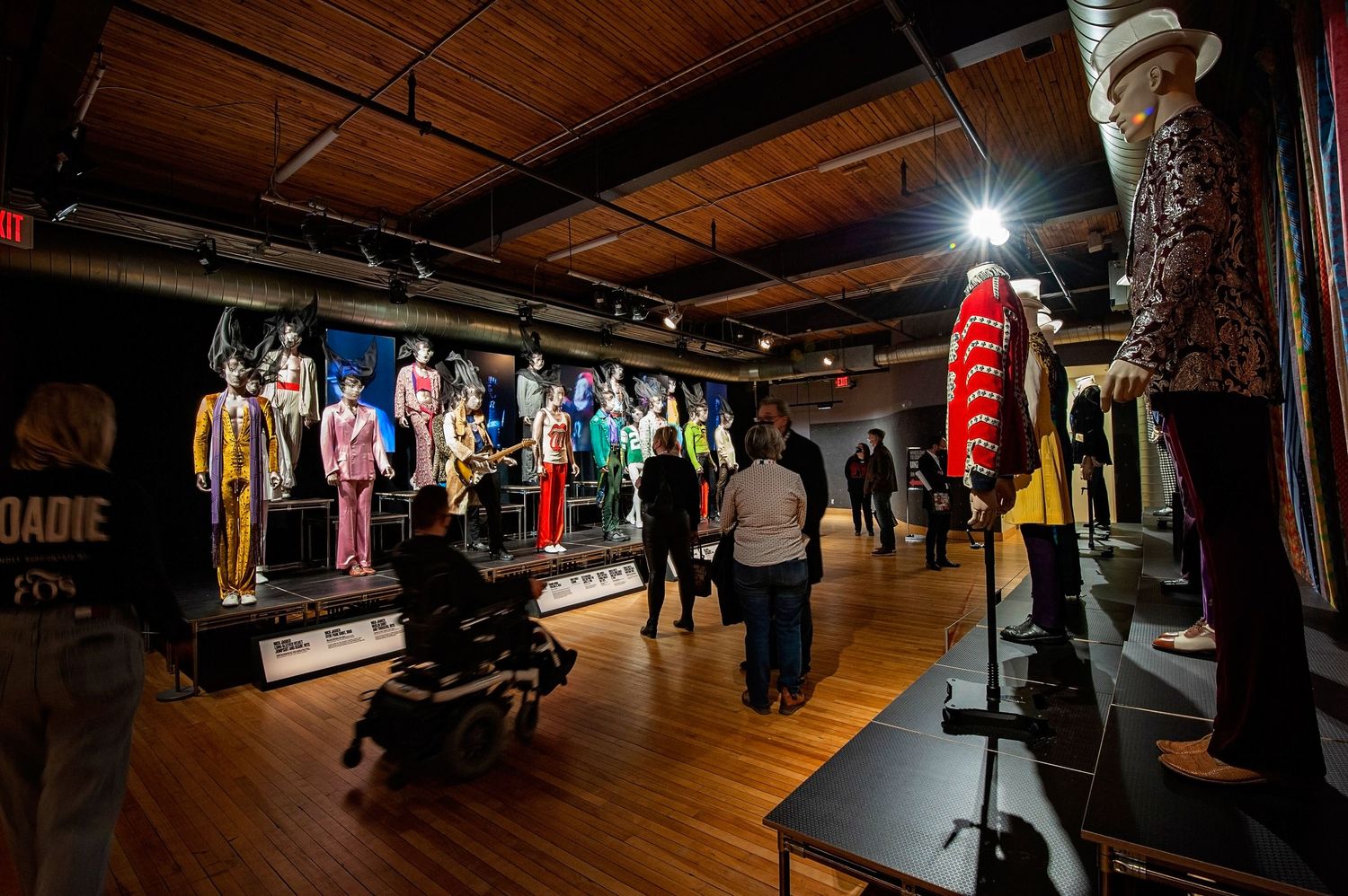 Visitors explore a rock music exhibition featuring iconic stage costumes on mannequins.