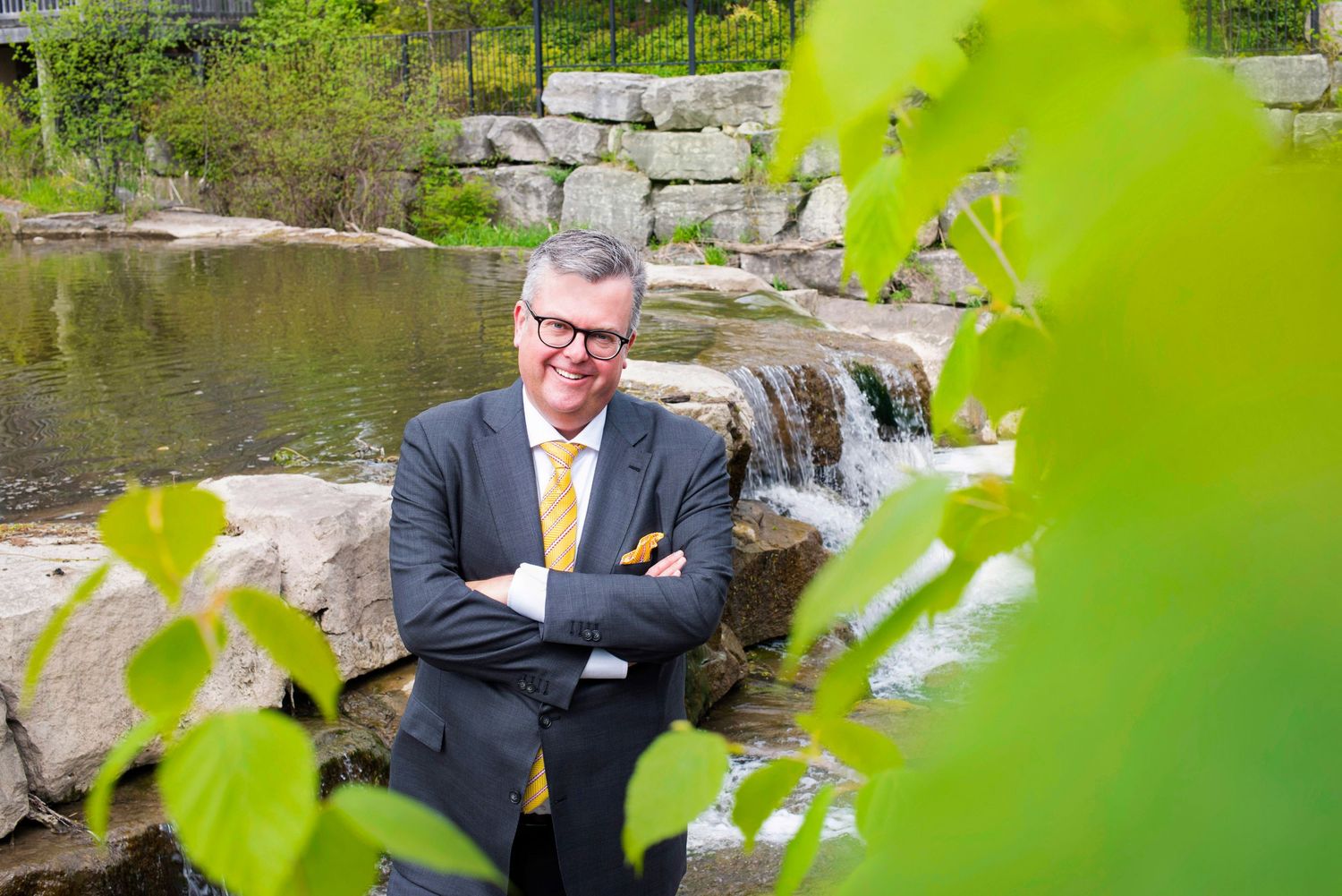 Smiling businessman in gray suit standing near waterfall garden feature outdoors.