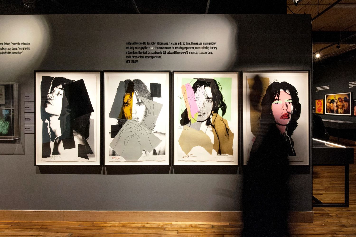 Museum visitor walks past Andy Warhol portraits of Rolling Stones members on display.