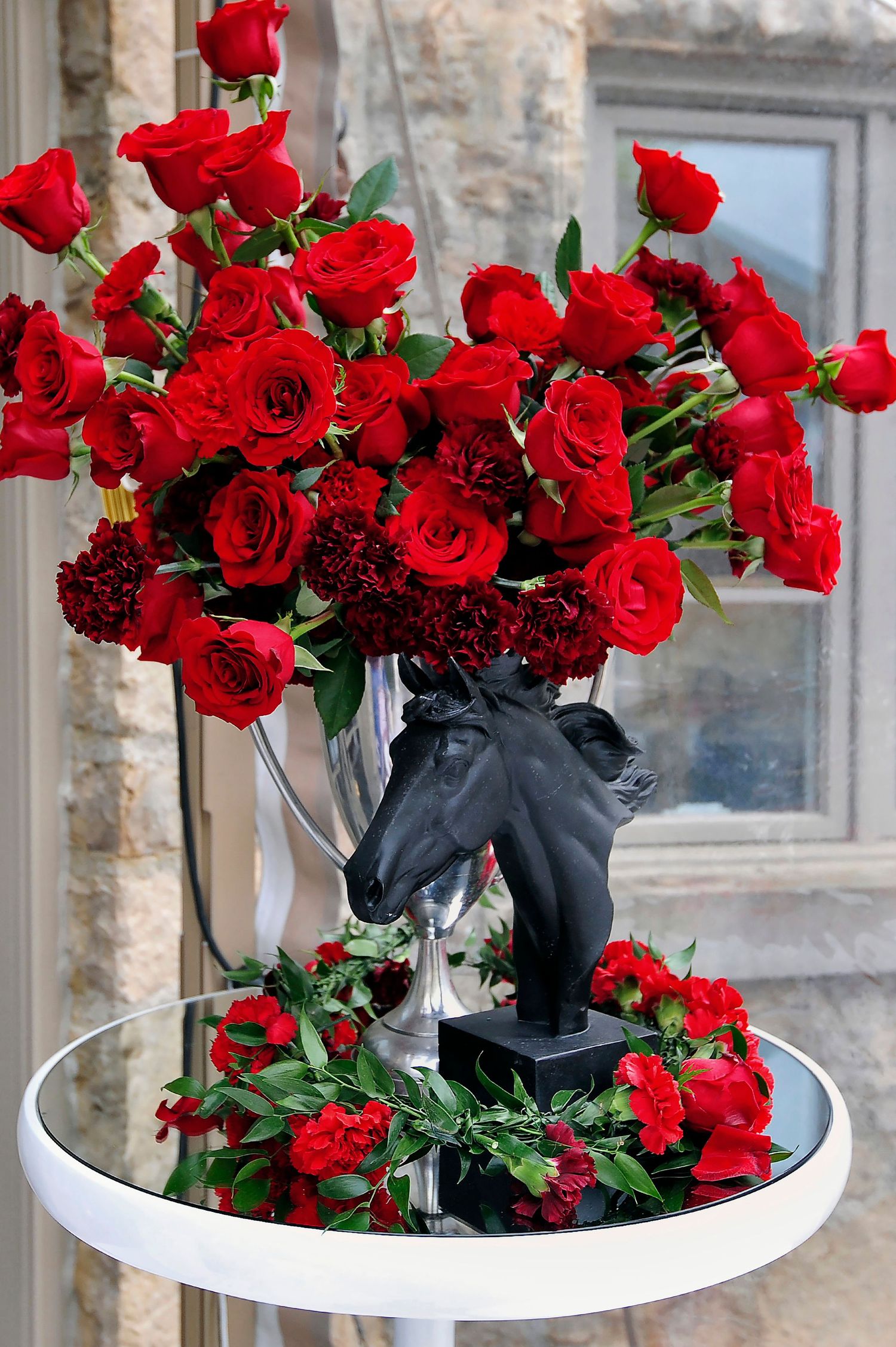Stunning red rose floral arrangement in silver horse head vase on white pedestal table for Kentucky Derby.