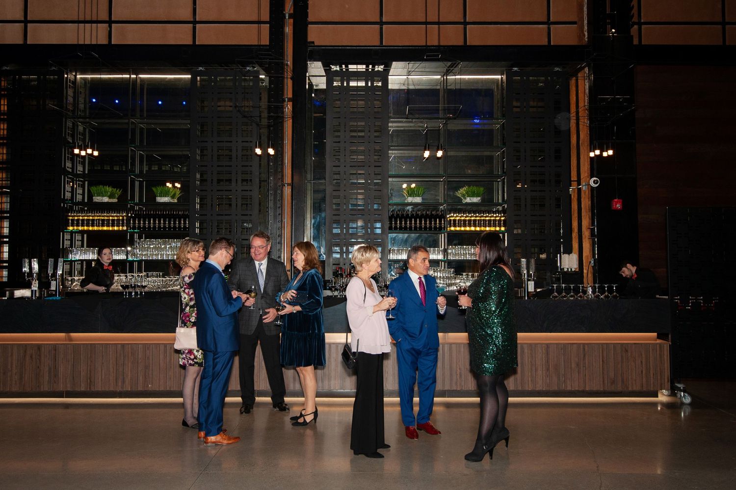 Small group of elegantly dressed guests socializing near a modern bar at an upscale evening event.