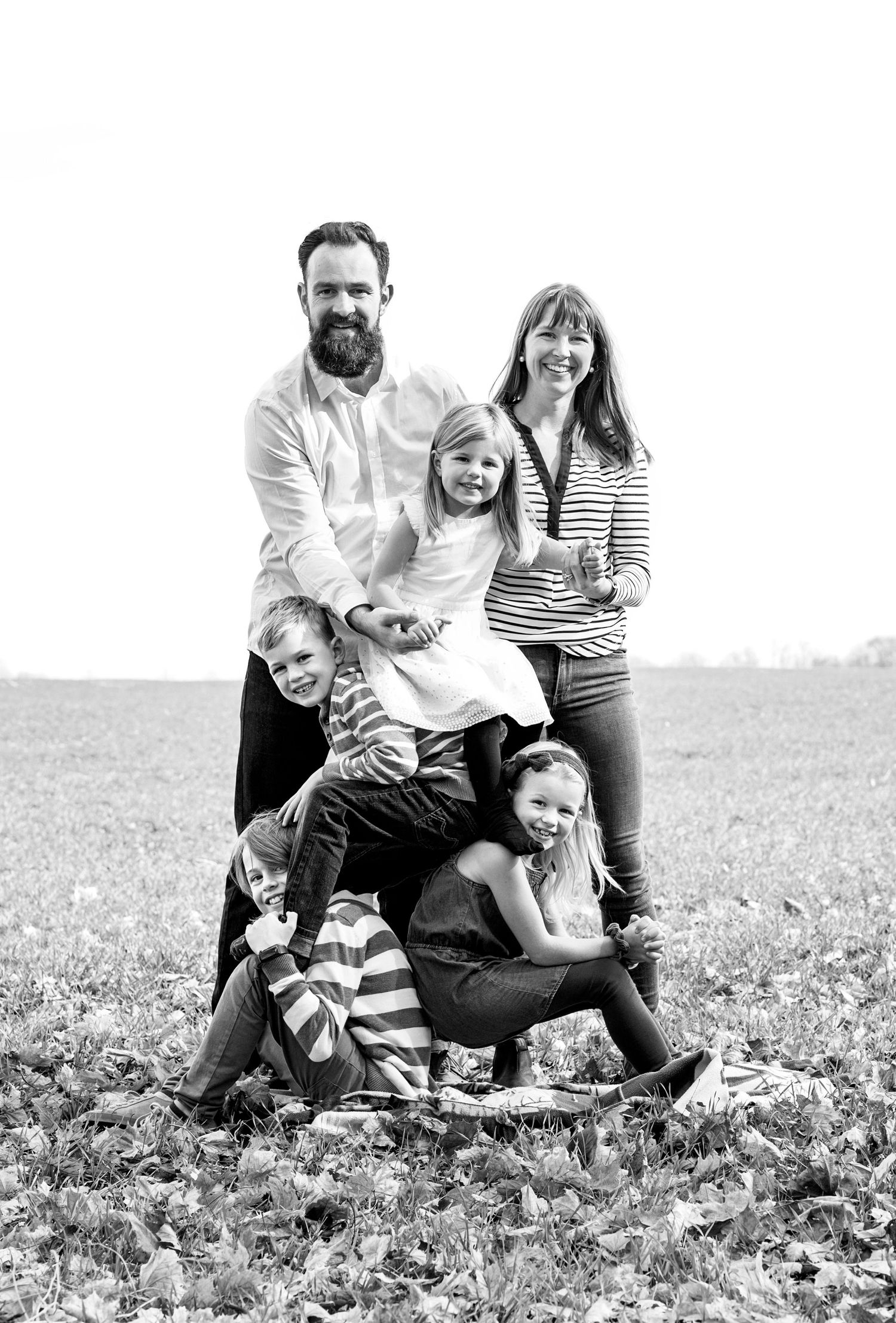Black and white portrait of a bearded father, mother, and four children posing playfully in a field.