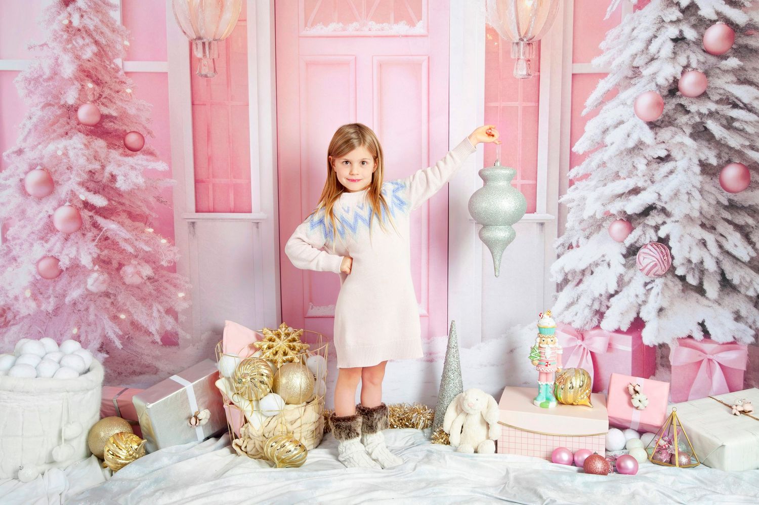 Young girl posing in pink Christmas studio with decorated trees and gifts.