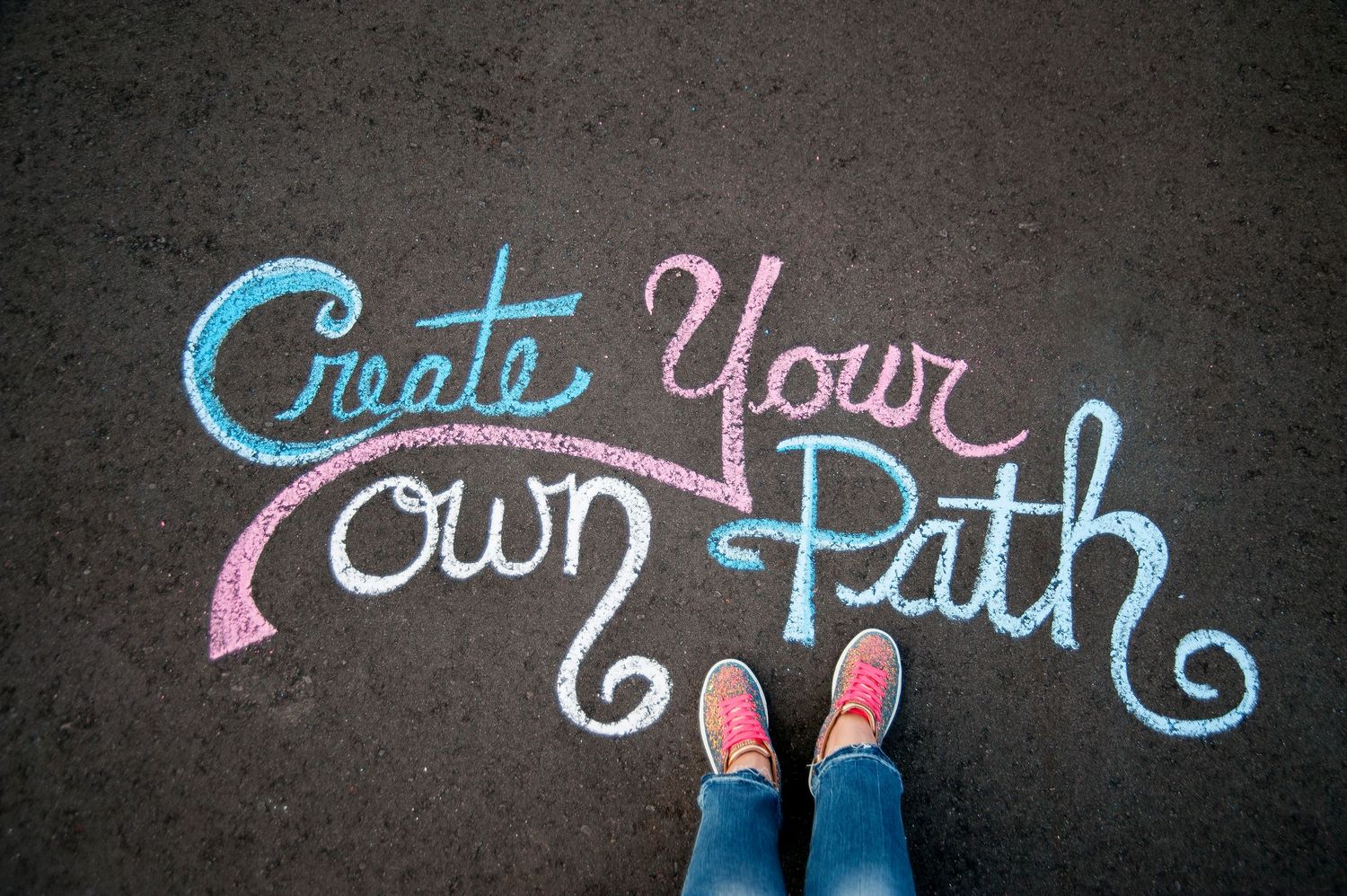 Overhead view of feet in pink sneakers standing above chalk lettering reading Create Your Own Path.