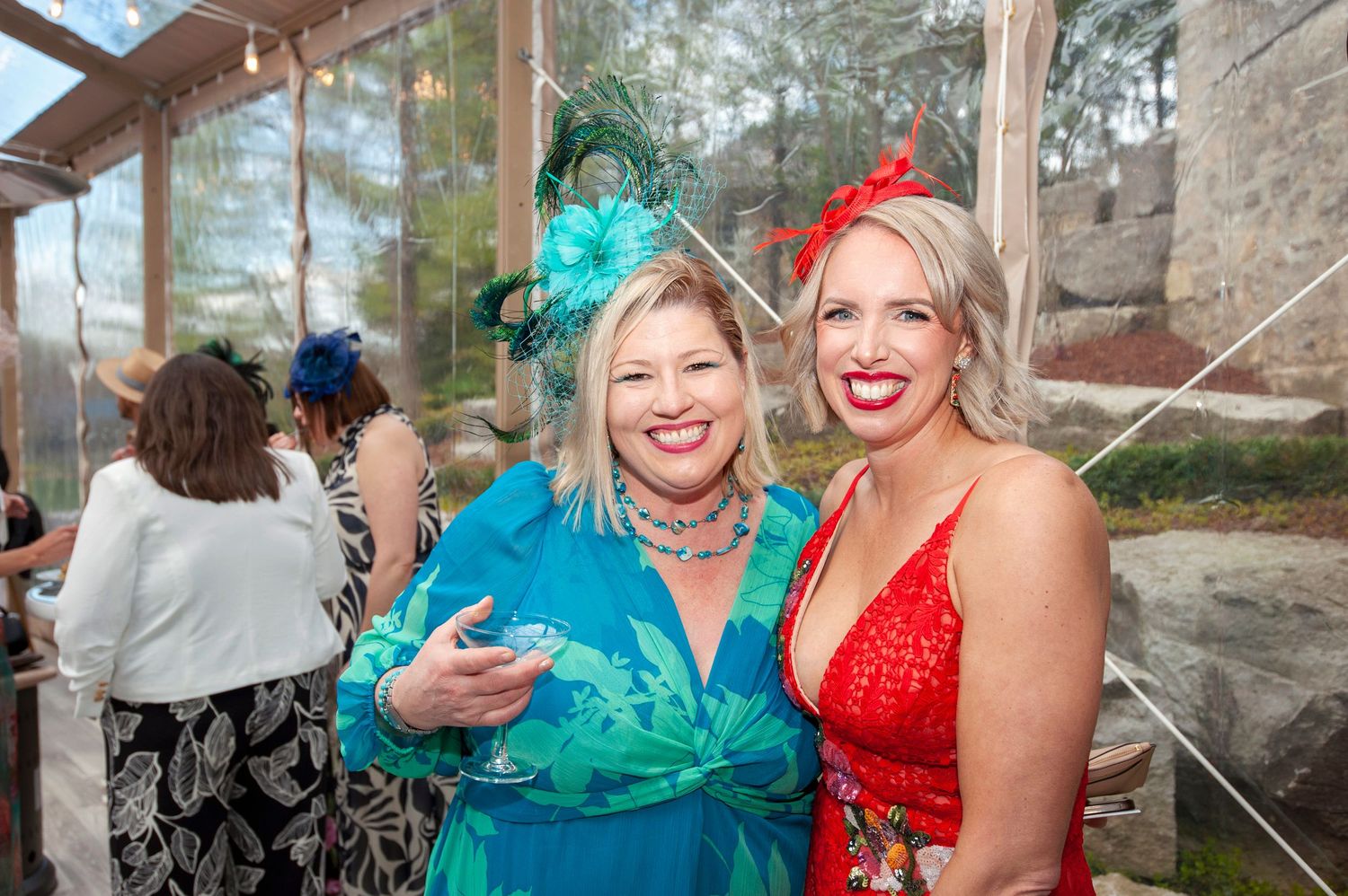 Two women in festive fascinators and colorful dresses posing together at an elegant Kentucky Derby party.