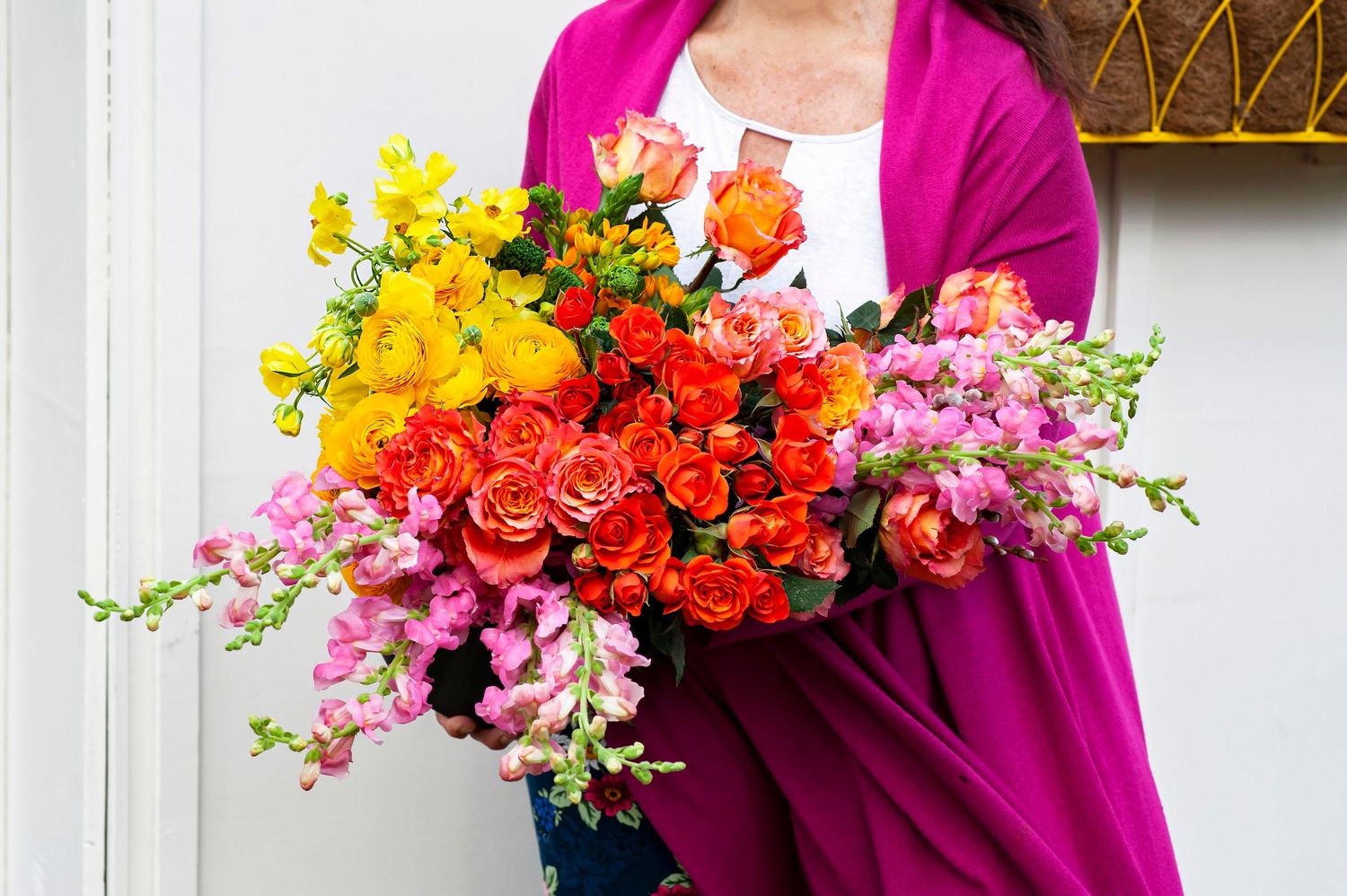 Woman in magenta cardigan holding large colorful bouquet of roses and mixed flowers.