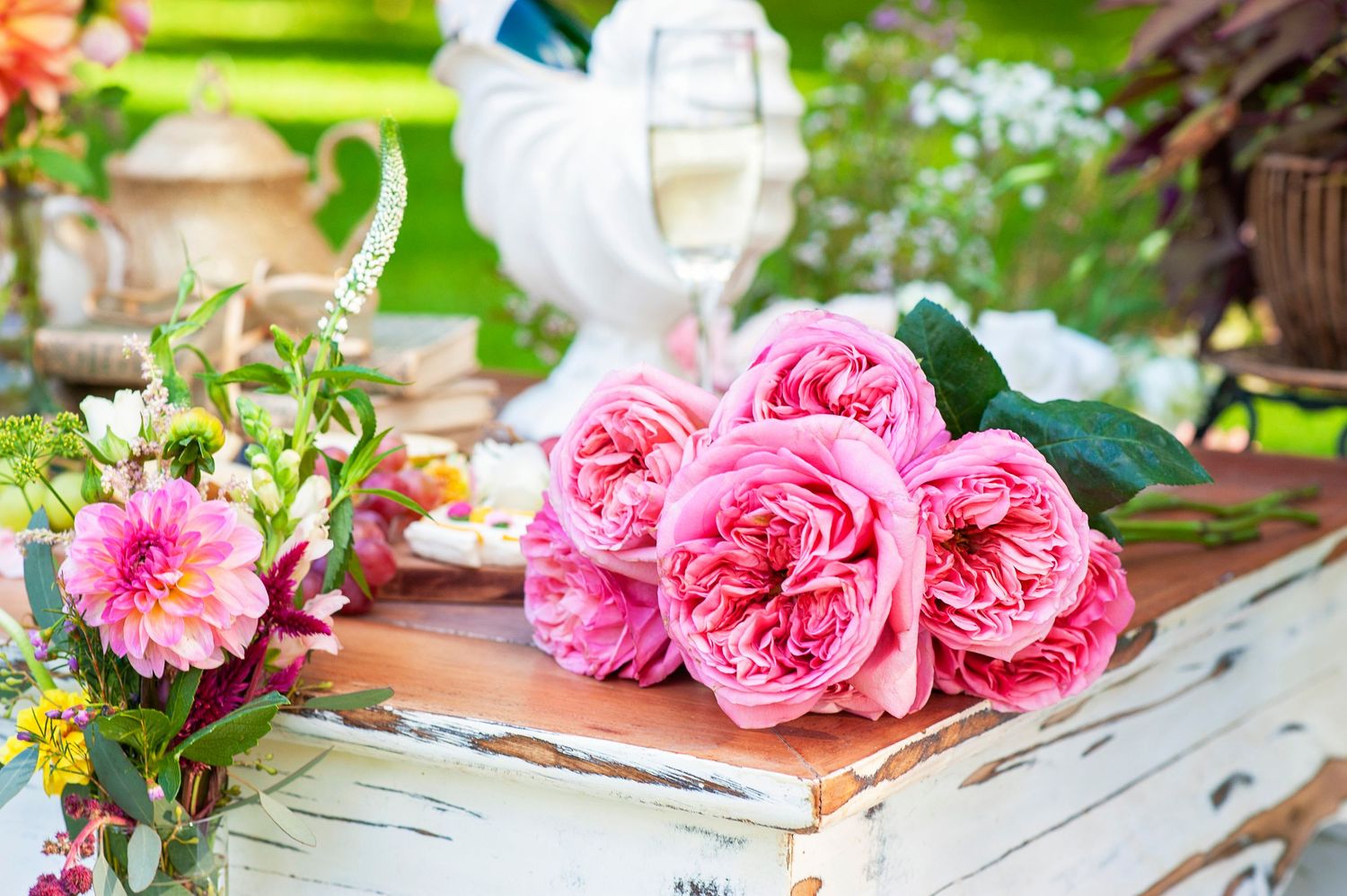 Pink roses bouquet on a rustic white wooden box at an outdoor garden party with champagne.