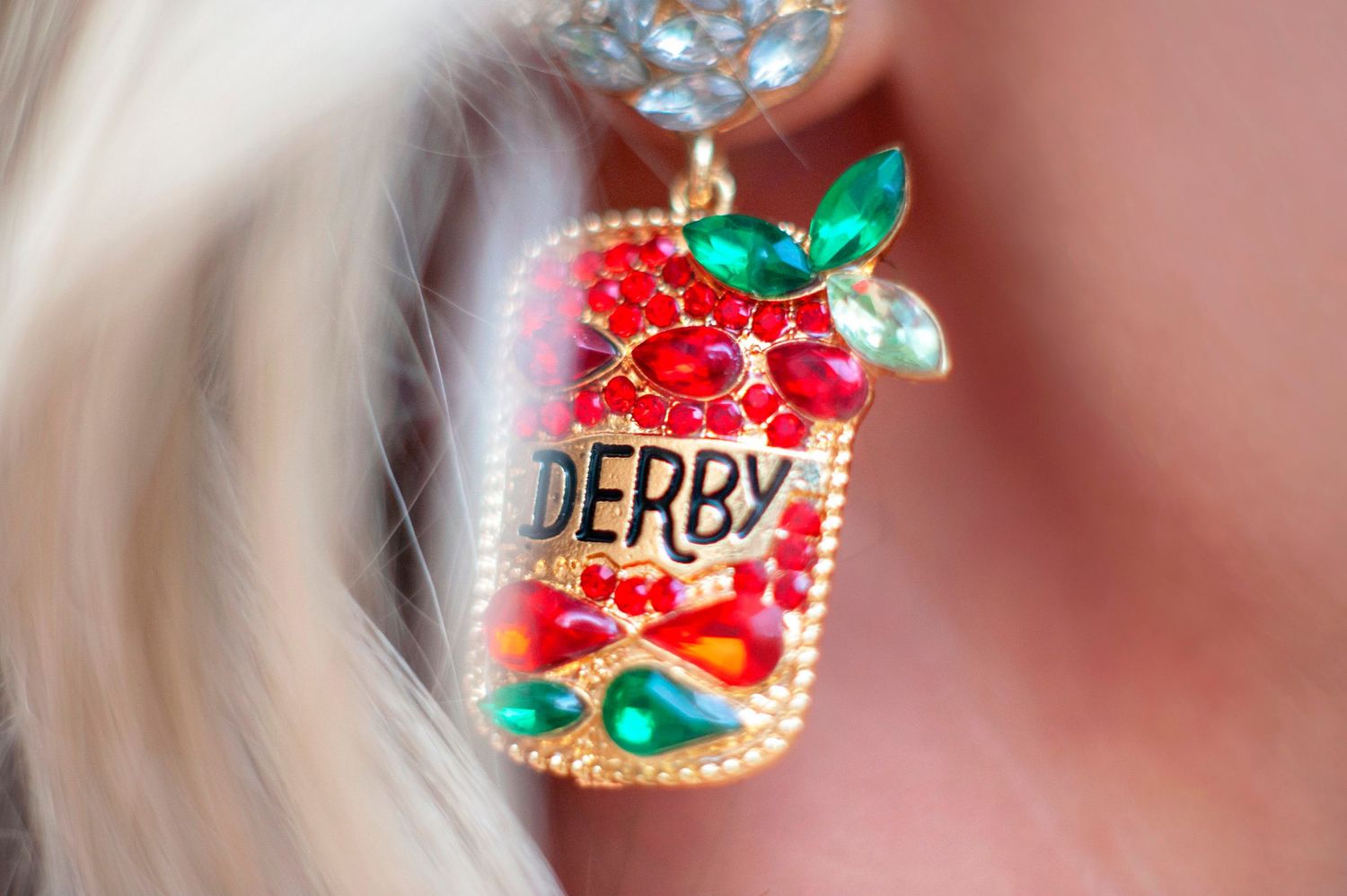 Colorful bejeweled Derby earring with red crystals and gold setting worn by blonde woman.