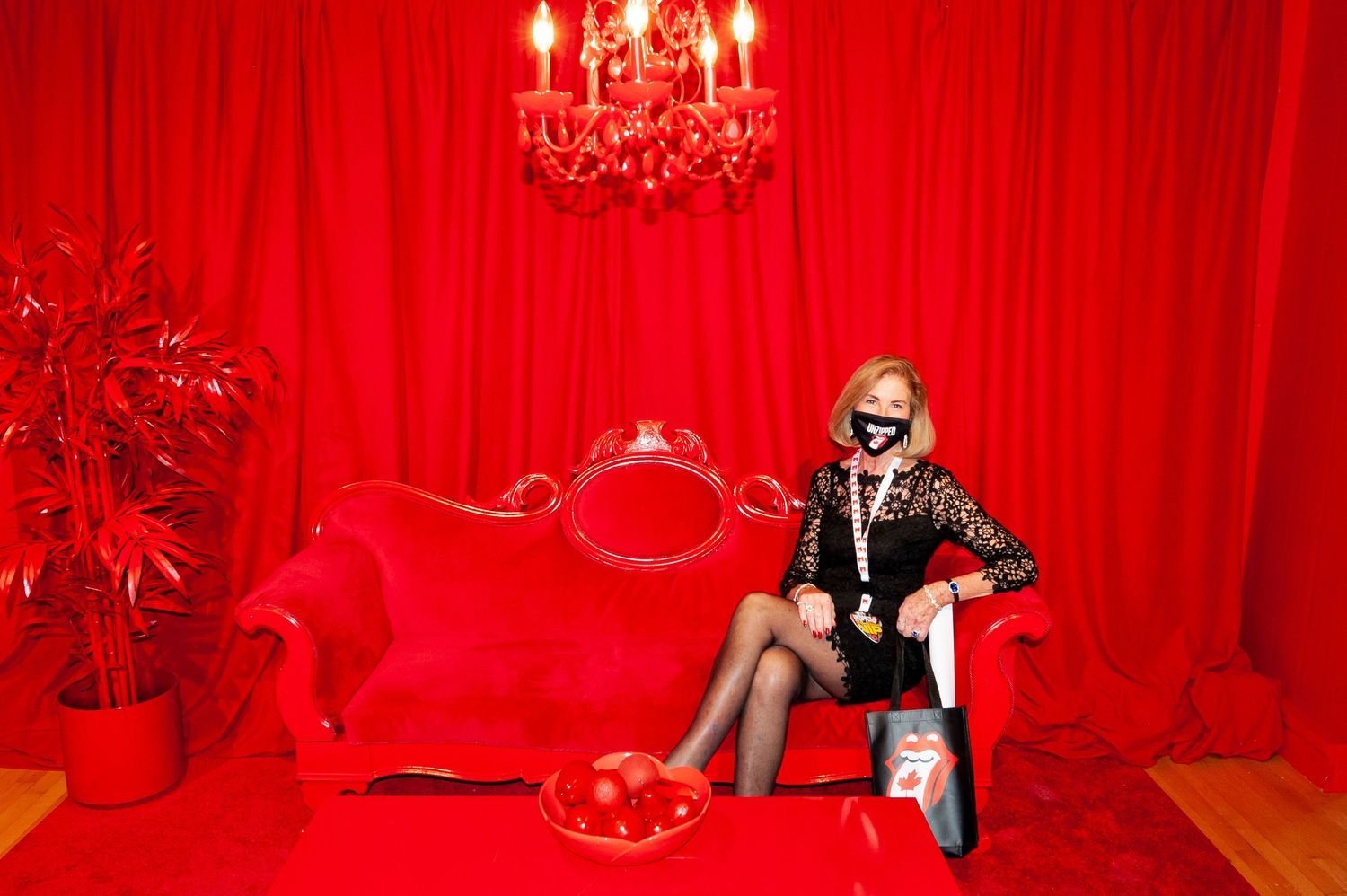Woman posing on red velvet sofa in an all-red themed Rolling Stones exhibition photo booth.