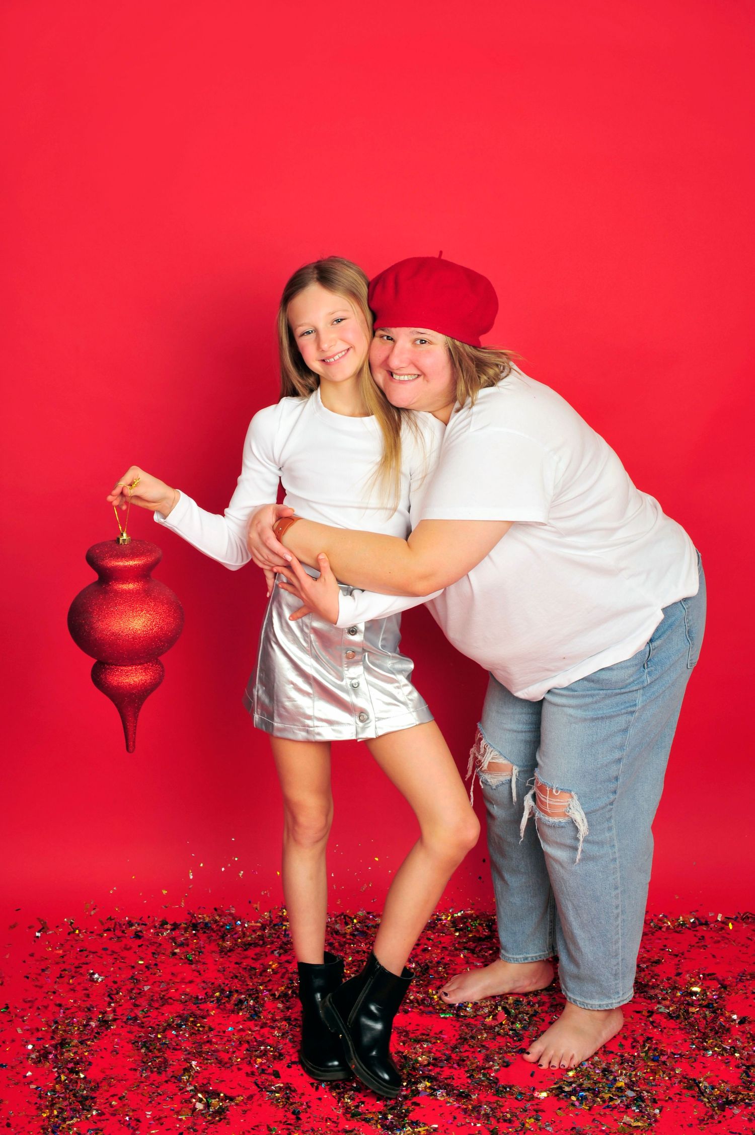 Aunt and niece in white tops hugging and smiling on red background with confetti.