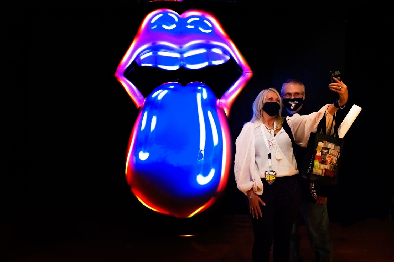 Two visitors take a selfie with the iconic Rolling Stones lips and tongue neon logo.