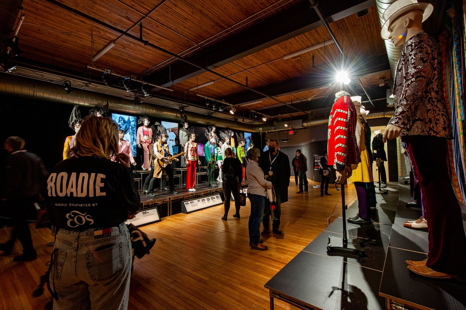 Visitors browse colorful stage costumes on display at a rock music exhibition.