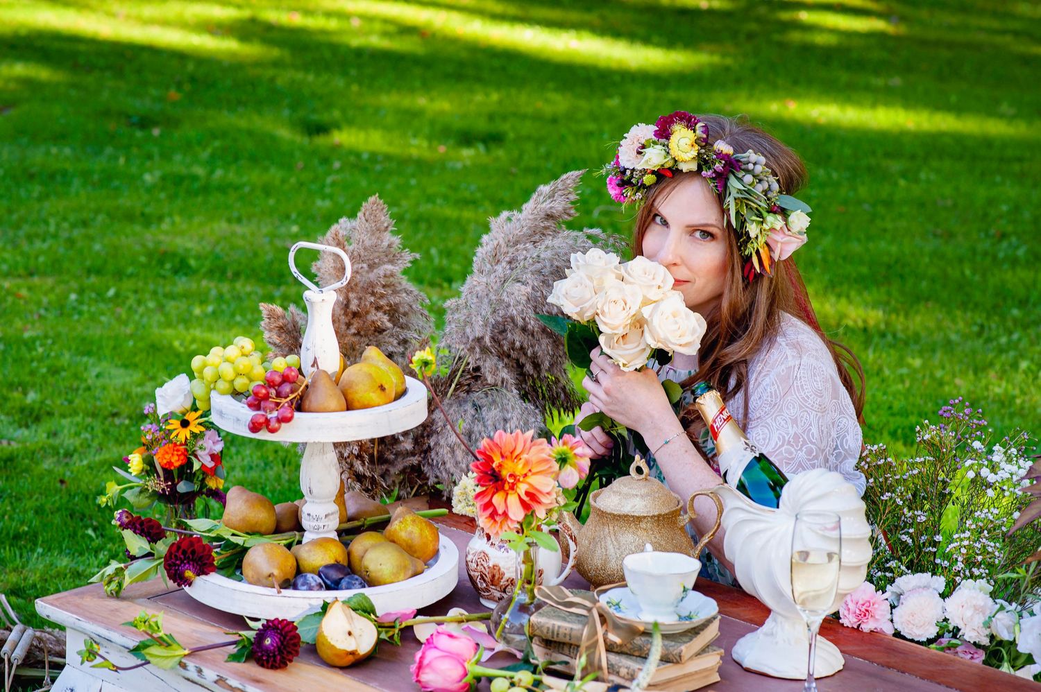 Young woman with flower crown smelling roses at an outdoor garden picnic table setting.