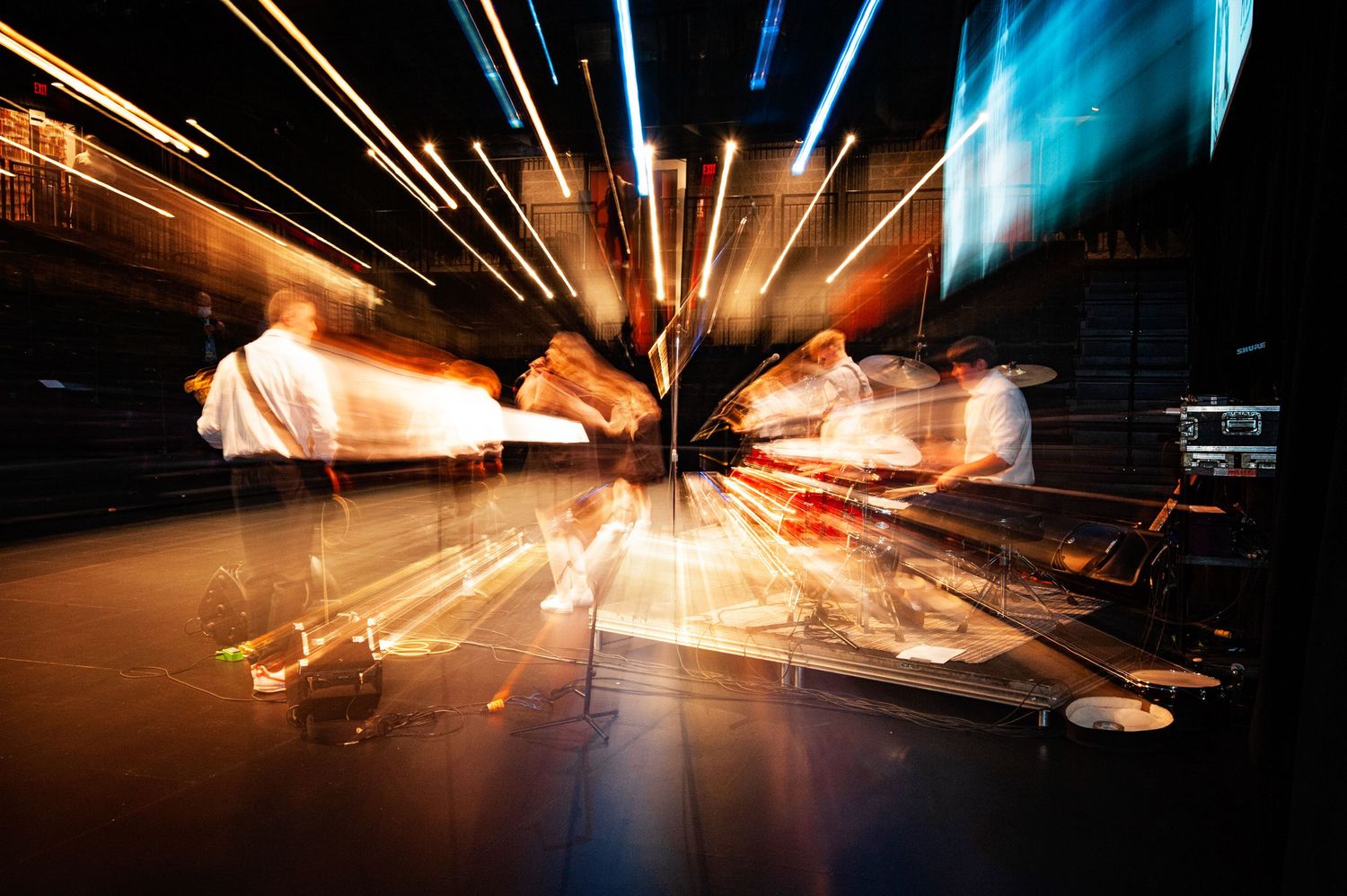 Blurred motion long exposure photo of musicians performing on a brightly lit stage.