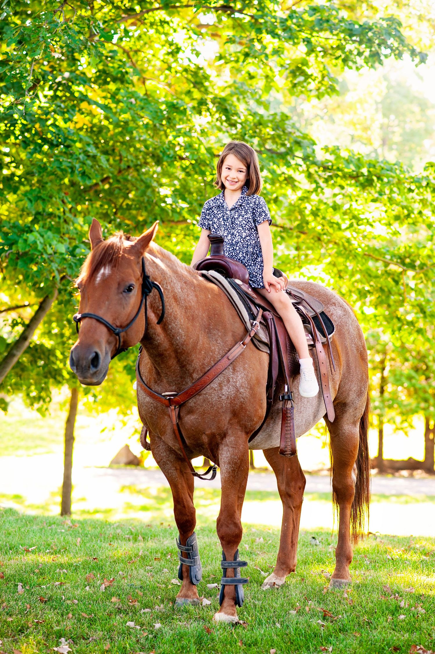 Young girl smiling while riding a chestnut horse in a green park.