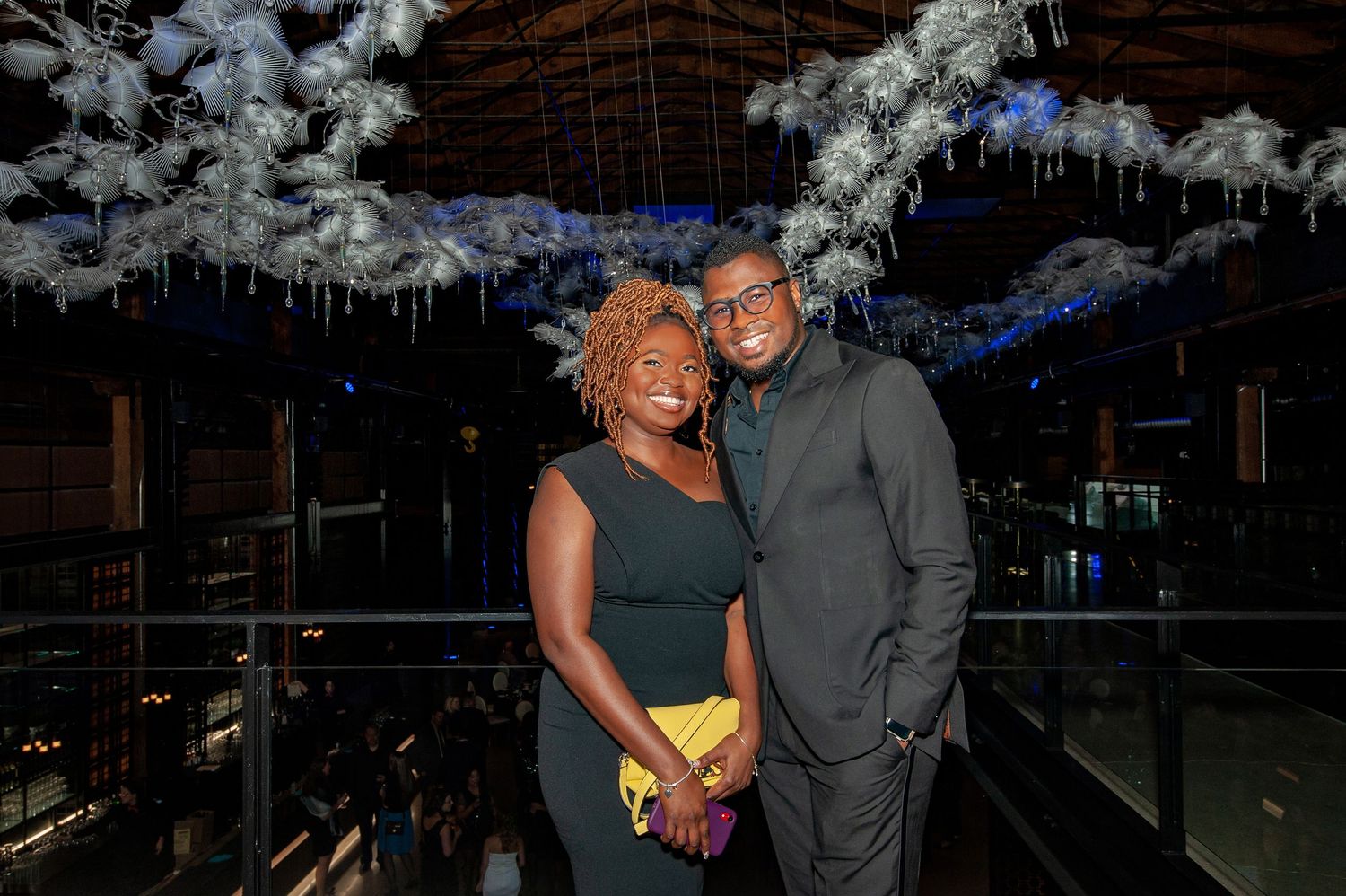 Smiling couple posing together under white winter-themed ceiling decor at an elegant gala event.