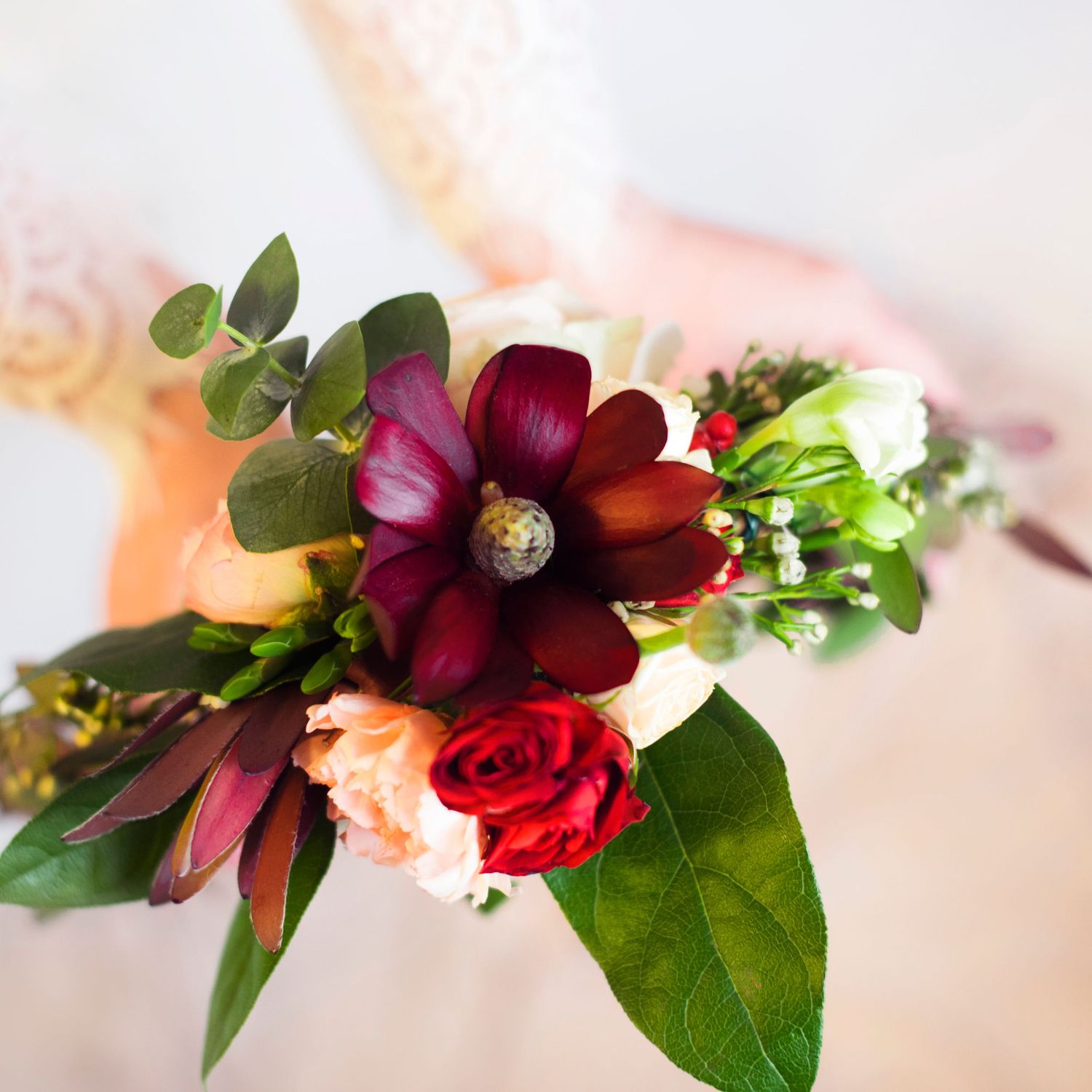 Close-up of a bouquet with burgundy dahlia, peach roses, and greenery against soft background.