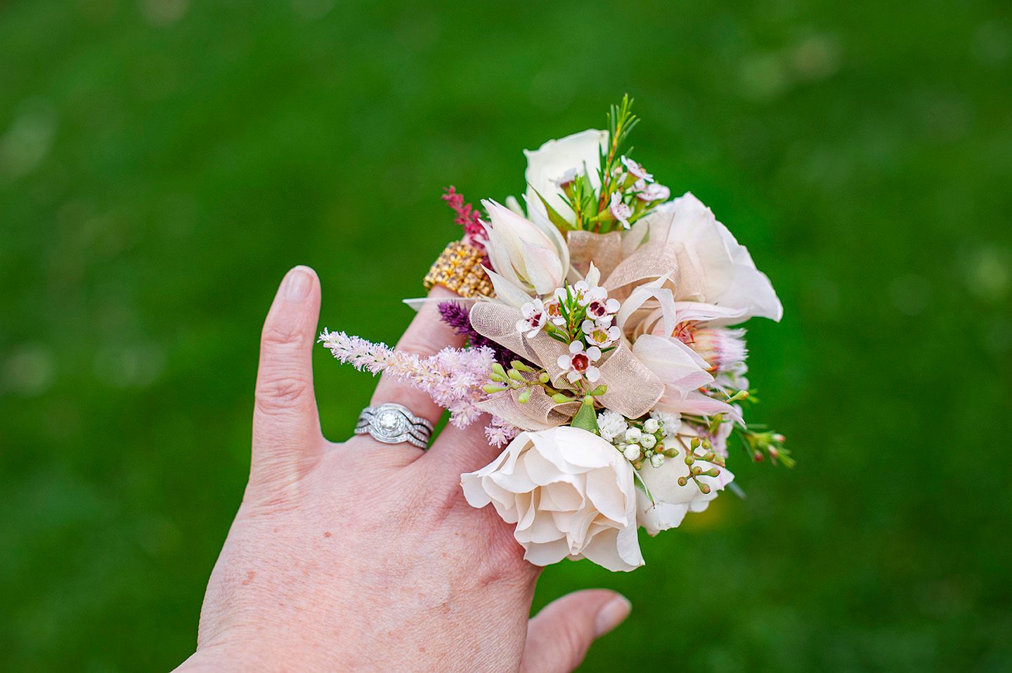 Hand wearing a silver ring holding a delicate blush pink and white floral wrist corsage outdoors.