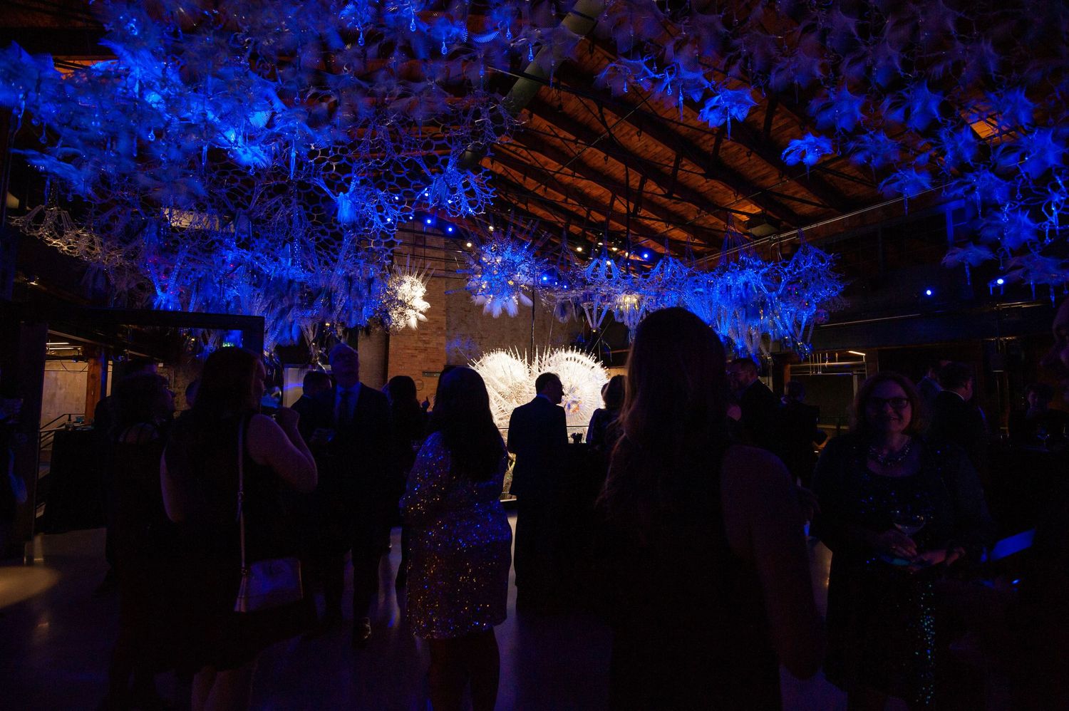 Guests mingling under dramatic blue-lit floral ceiling installation at an elegant evening reception.